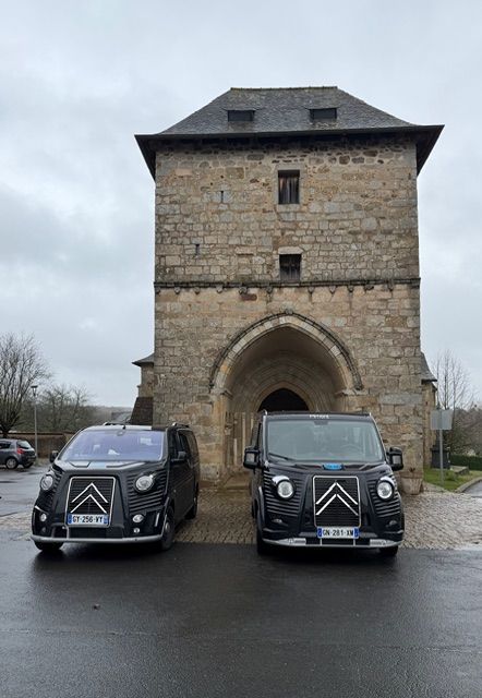 Deux fourgonnettes noires garées devant le portail d'une tour en pierre par une journée nuageuse