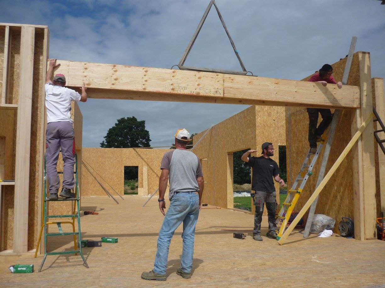 Des ouvriers sur un chantier en train de poser une grande poutre en bois