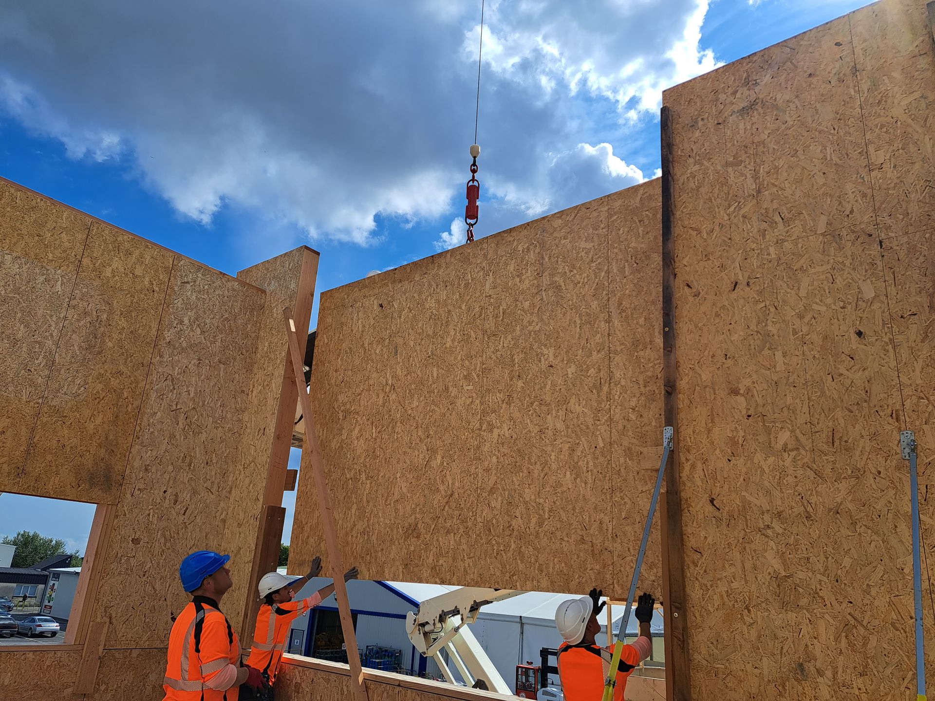 Plusieurs ouvriers en train de guider la pose d'un grand pan de mur tenu à l'aide d'une grue