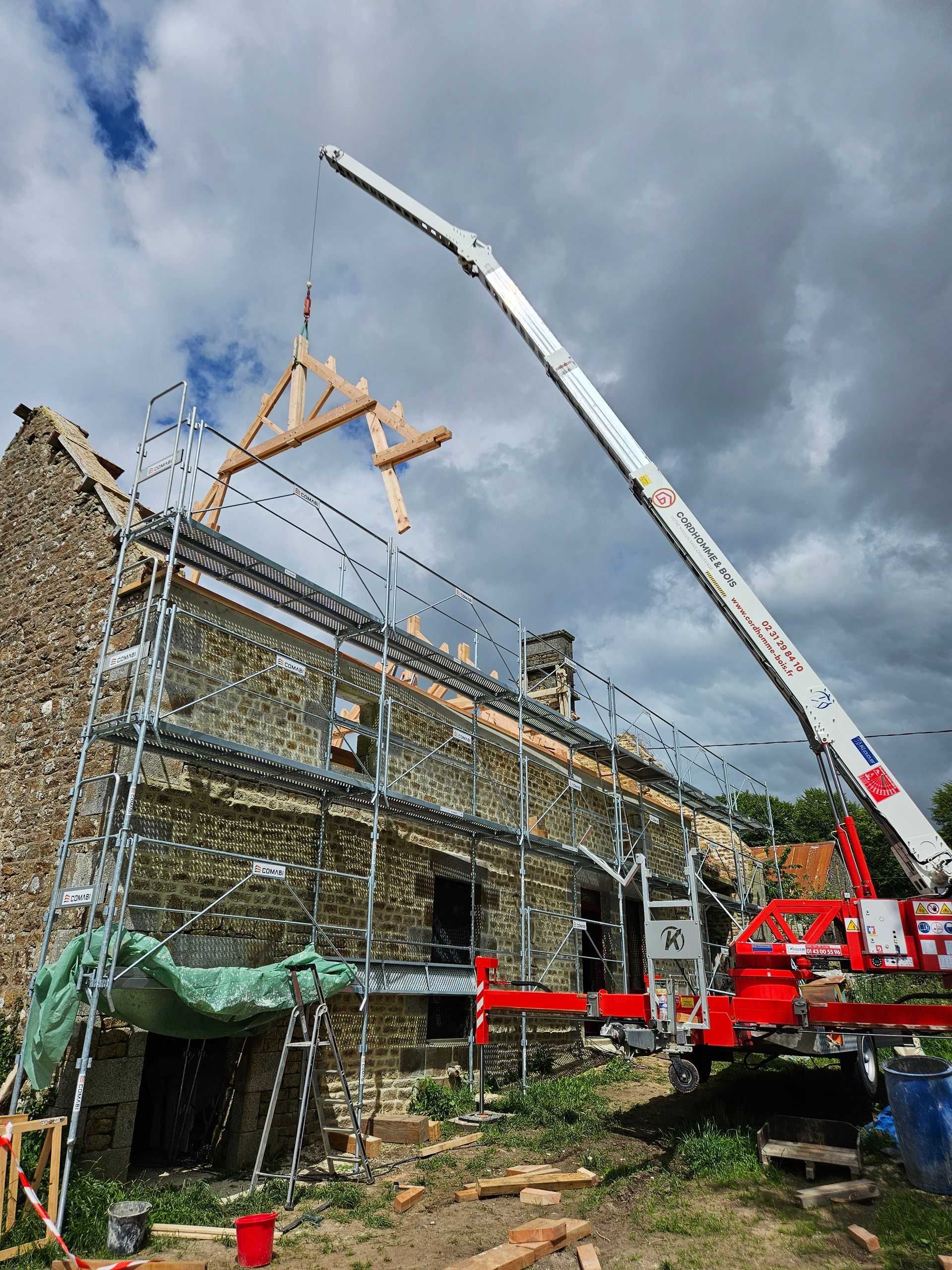Une grue en train de soulever une ossature en bois au-dessus d'un bâtiment en pierre