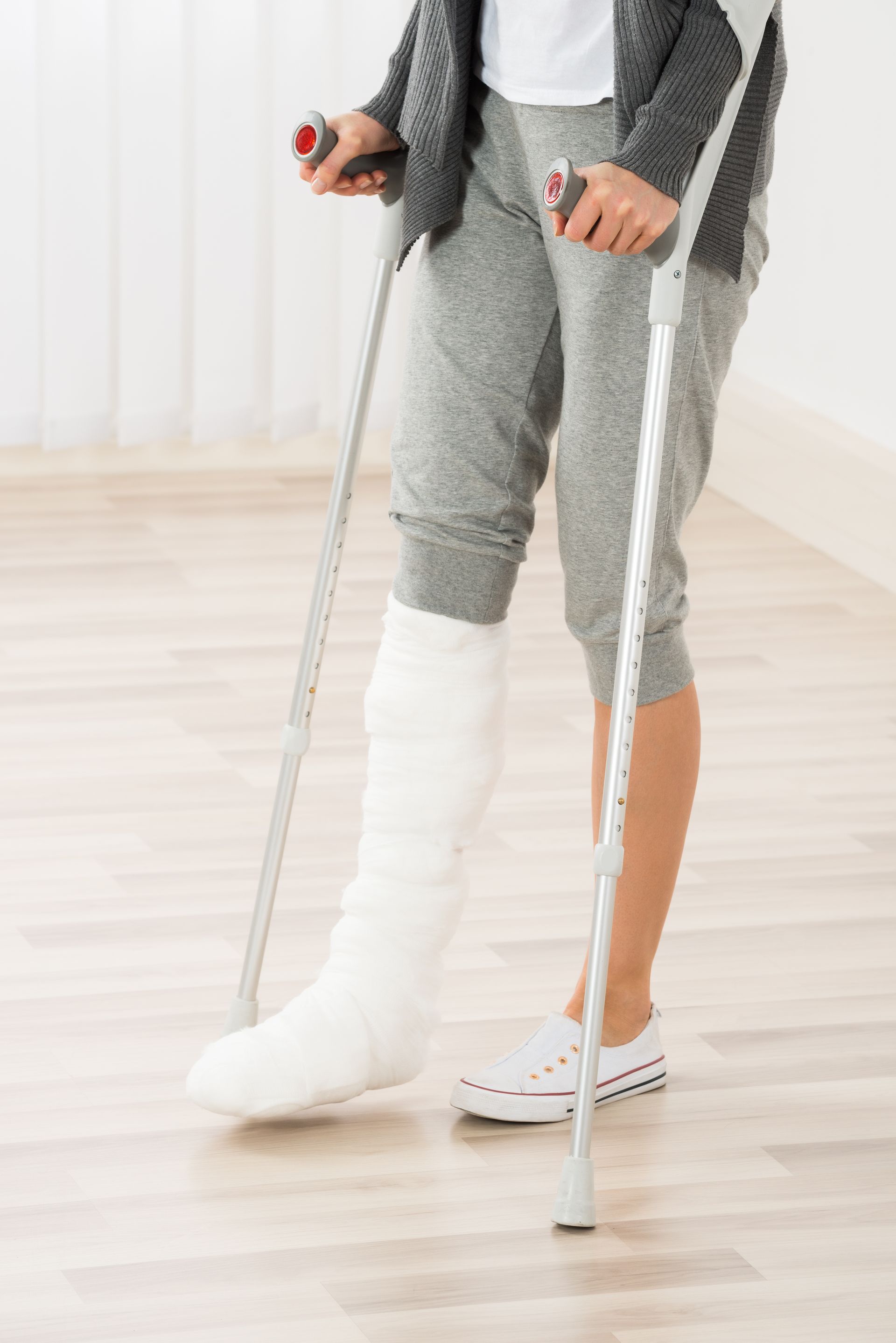 Personne avec une jambe plâtrée utilisant des béquilles pour marcher sur un plancher en bois.