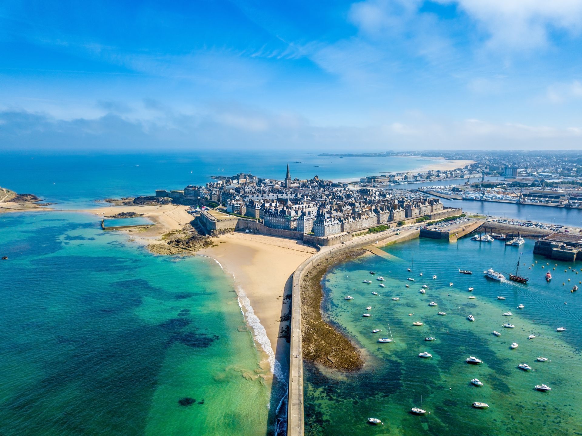 Vue aérienne de Saint-Malo, en France, une ville côtière fortifiée aux eaux turquoise, avec une plage de sable et des bateaux.