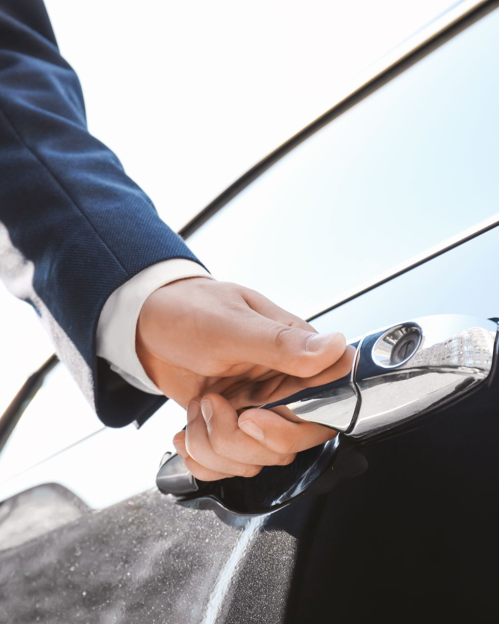 Main d'une personne en costume ouvrant une portière de voiture, à l'extérieur.
