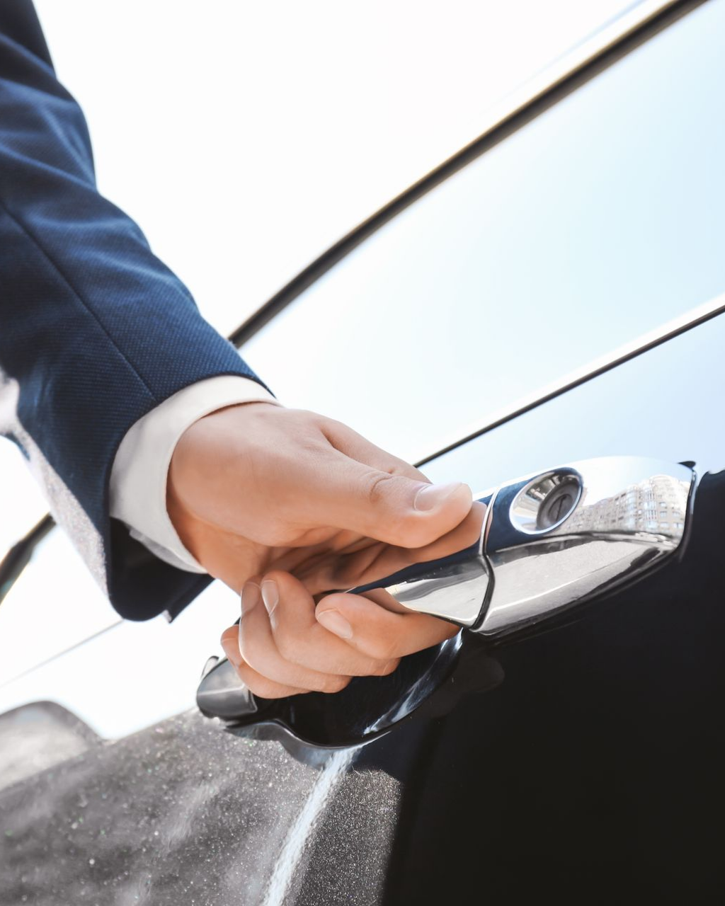 Une personne en costume ouvre une portière de voiture, gros plan sur la main et la poignée.