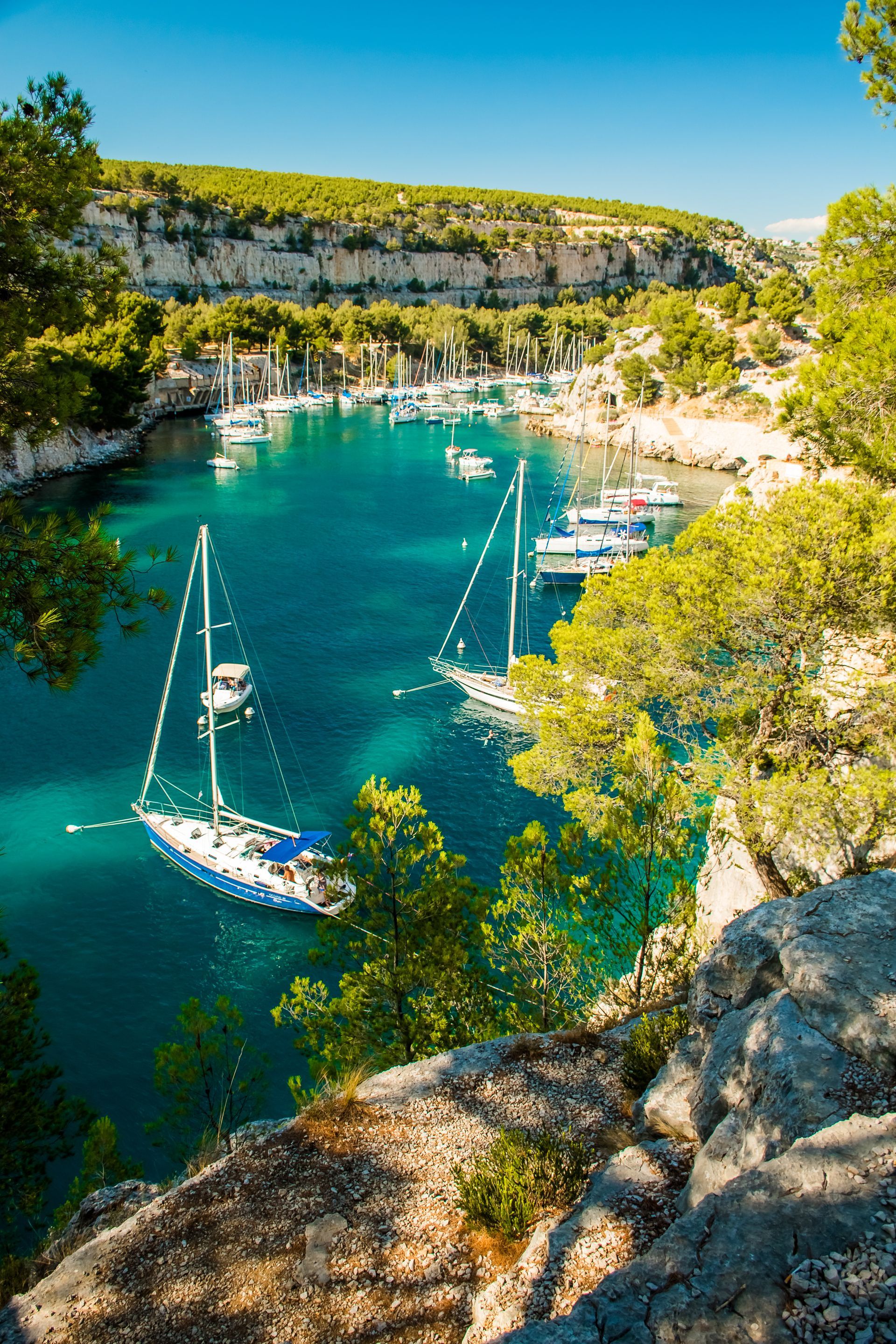 Des voiliers dans une baie turquoise, entourés de falaises et d'une végétation luxuriante sous un ciel d'un bleu éclatant.
