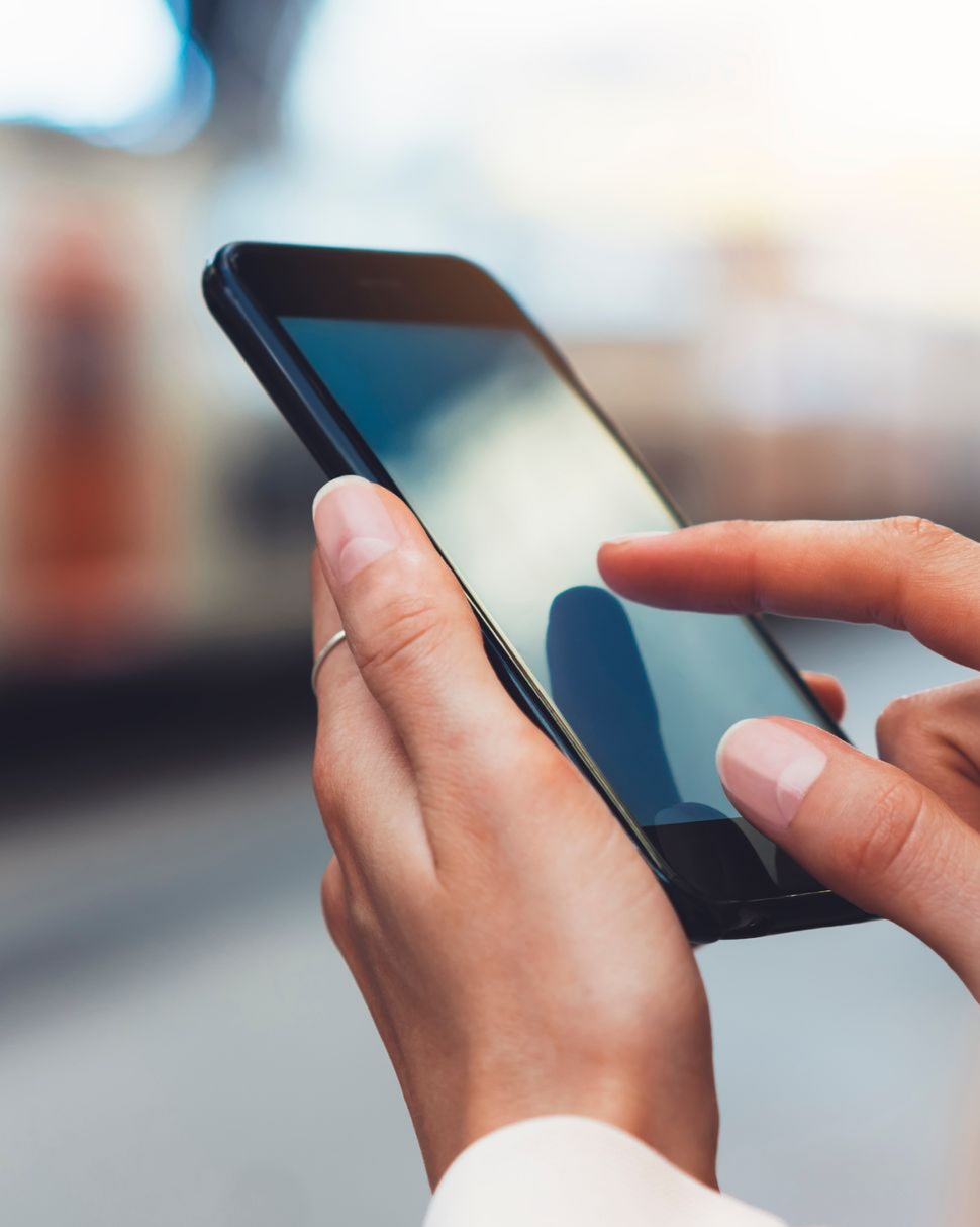 Main d'une personne utilisant un smartphone noir ; doigt touchant l'écran. Arrière-plan flou.