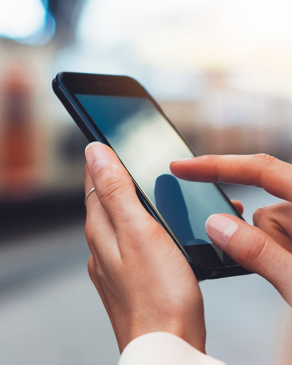 Main tenant un smartphone noir, doigt touchant l'écran à l'extérieur.