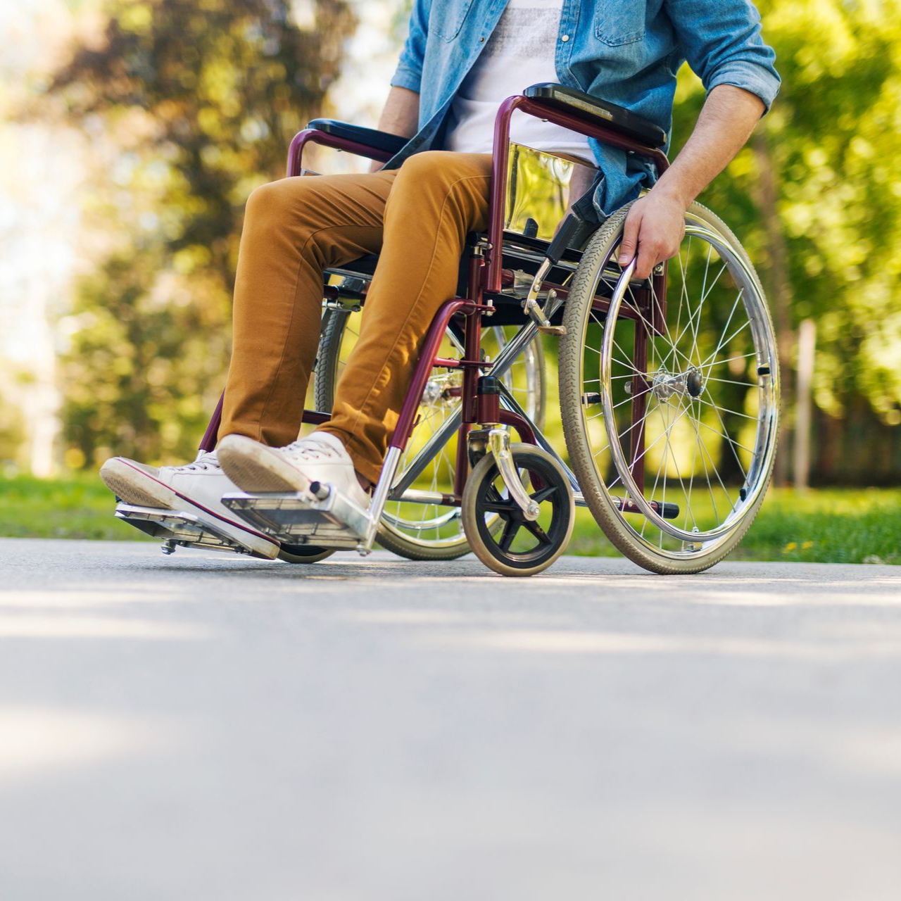 Personne en fauteuil roulant sur un chemin pavé à l'extérieur, portant un jean et un pantalon marron.