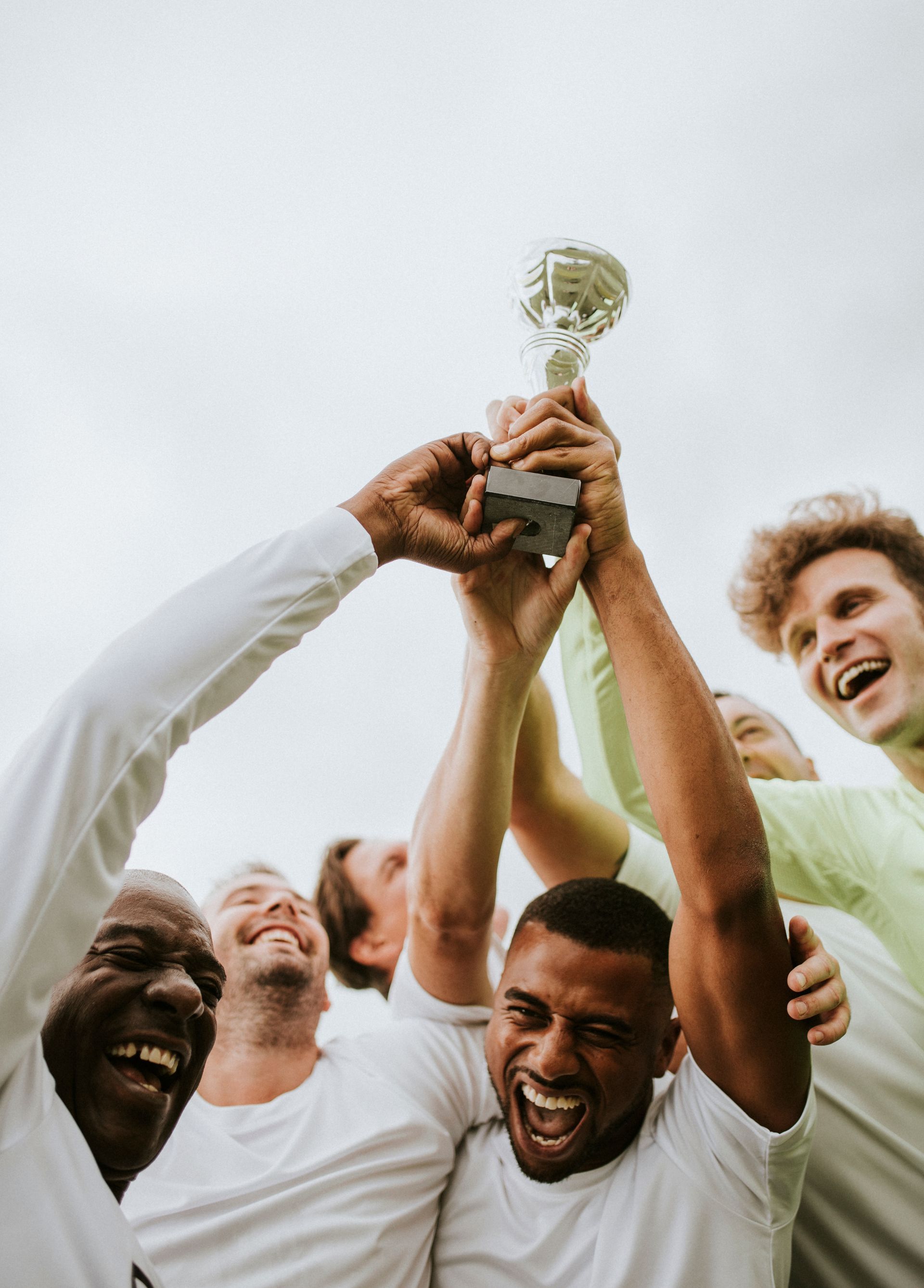 Des personnes brandissent un trophée, célébrant une victoire. Ciel en arrière-plan, sourires, expressions de joie et de triomphe.