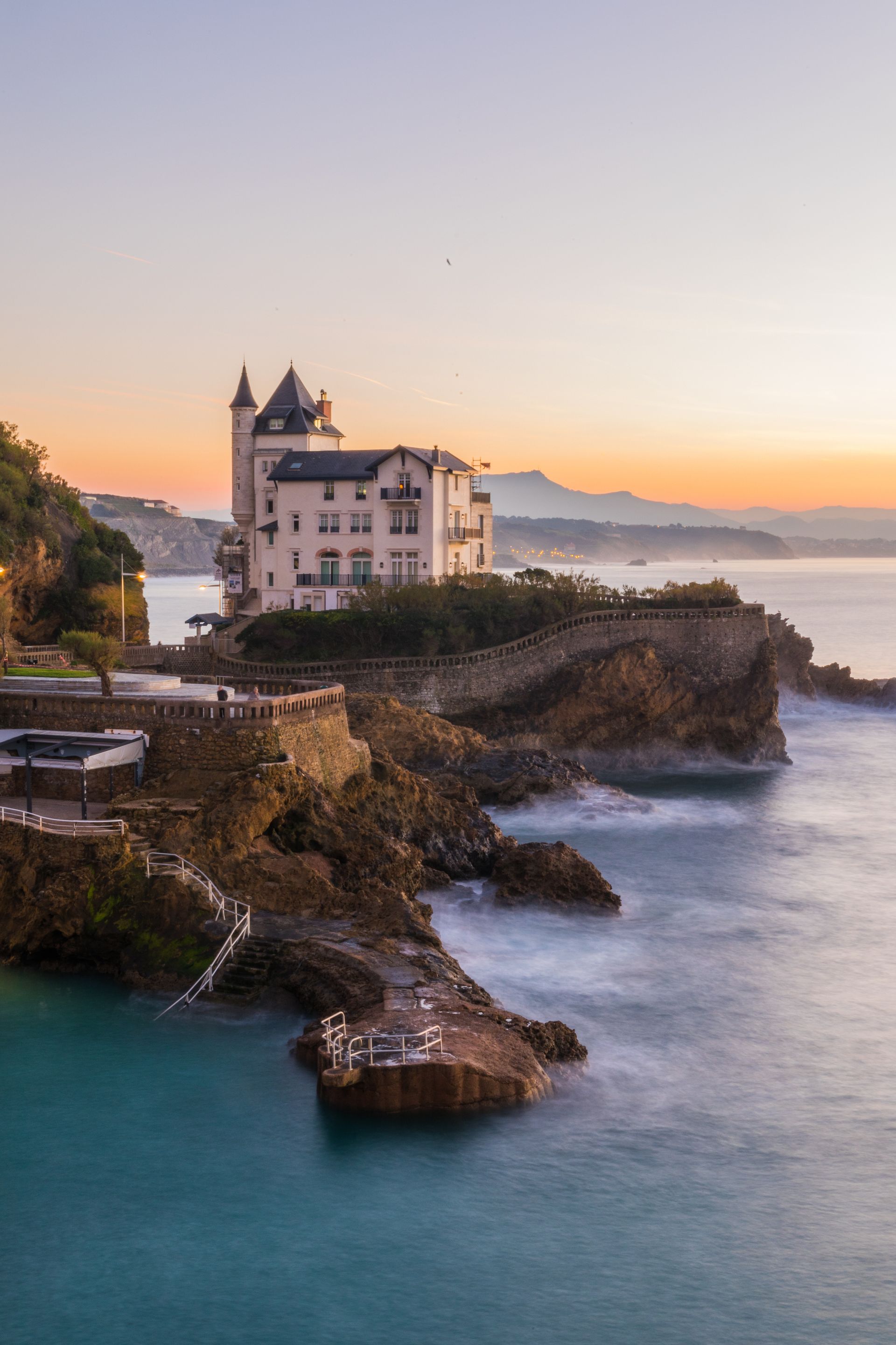 Bâtiment côtier sur un promontoire rocheux avec vagues et lever de soleil à Biarritz, France.