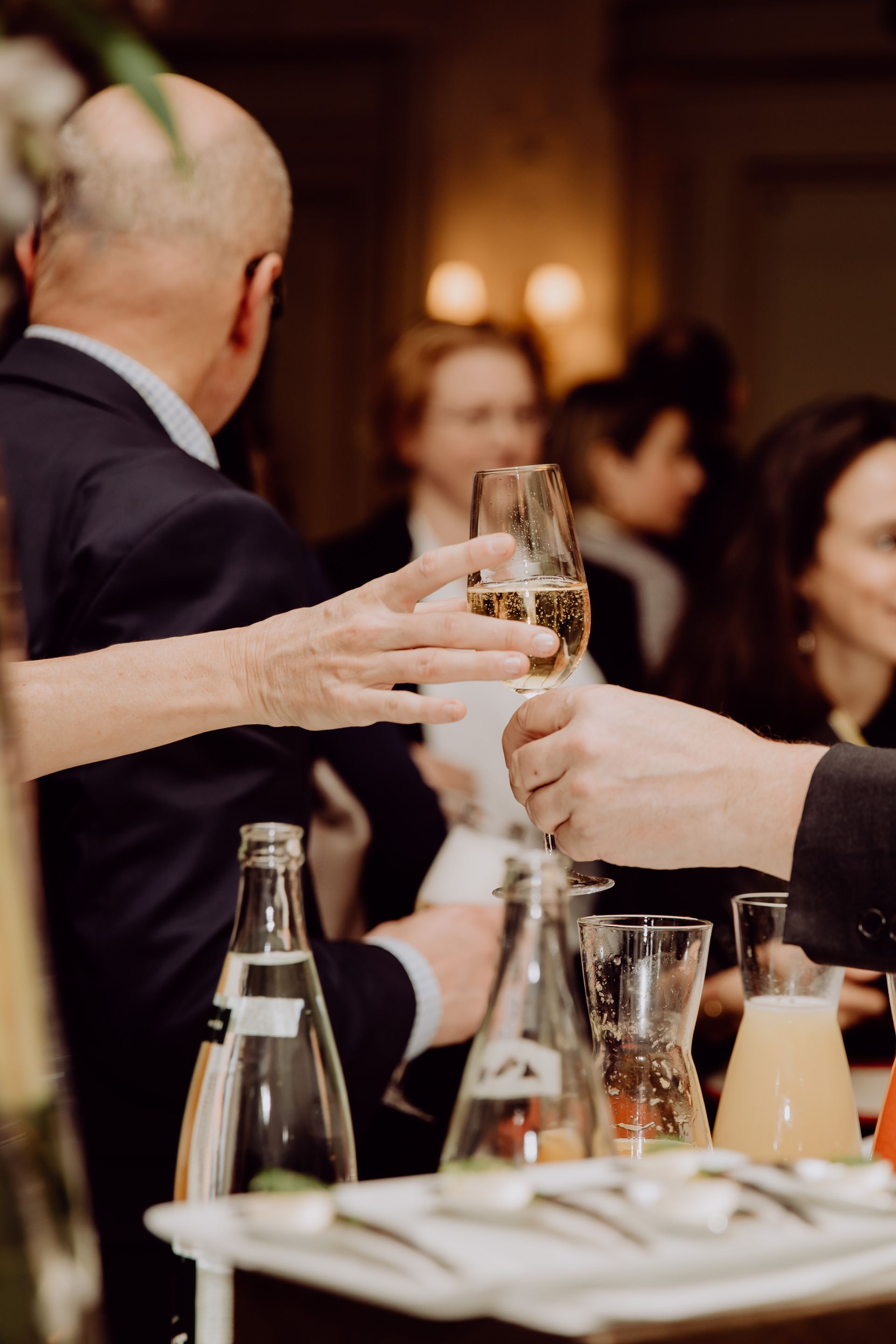 Des personnes trinquent avec des coupes de champagne lors d'un événement, entourées de bouteilles et de verres.