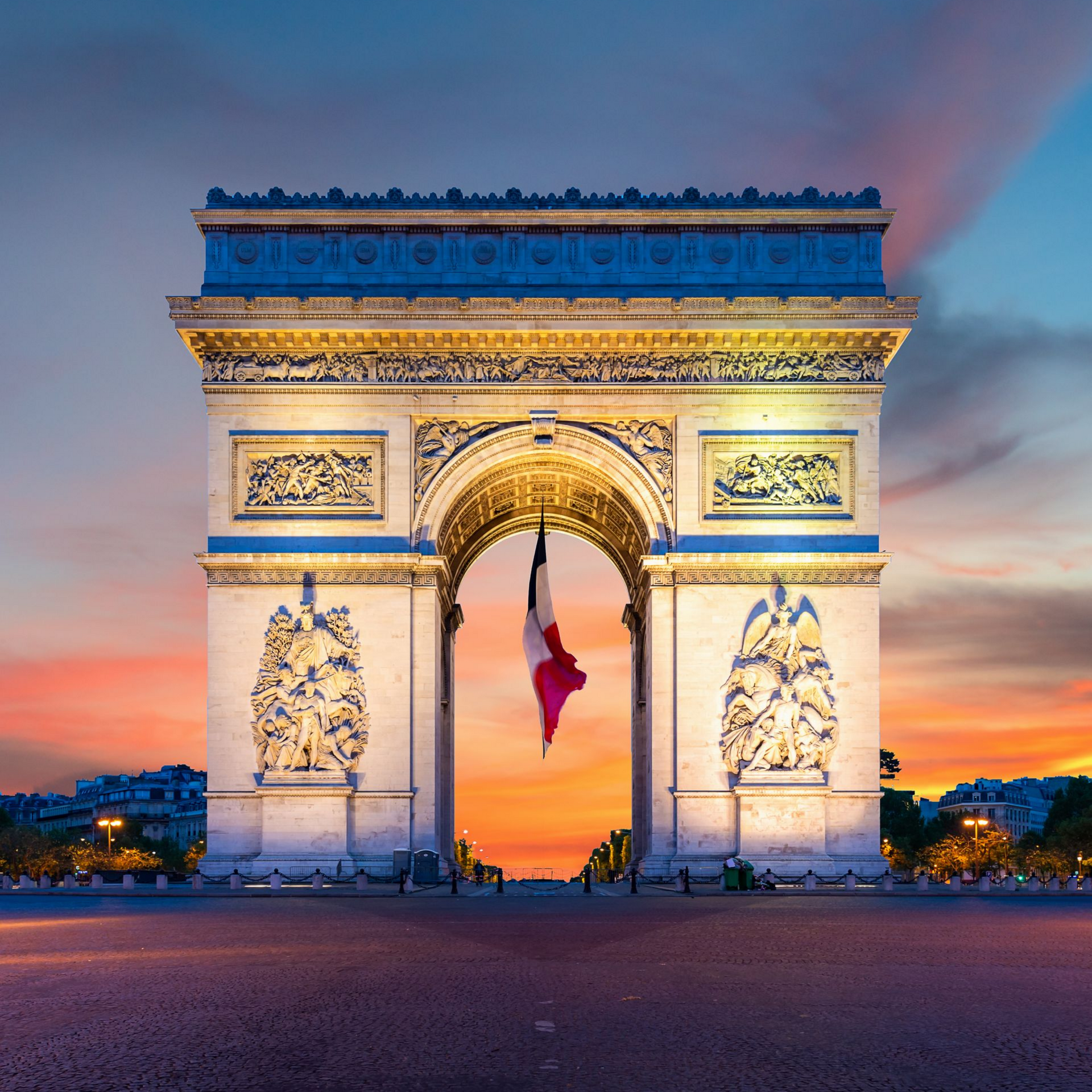 L'Arc de Triomphe à Paris, en France, avec le drapeau français qui y flotte, au crépuscule, au coucher du soleil.