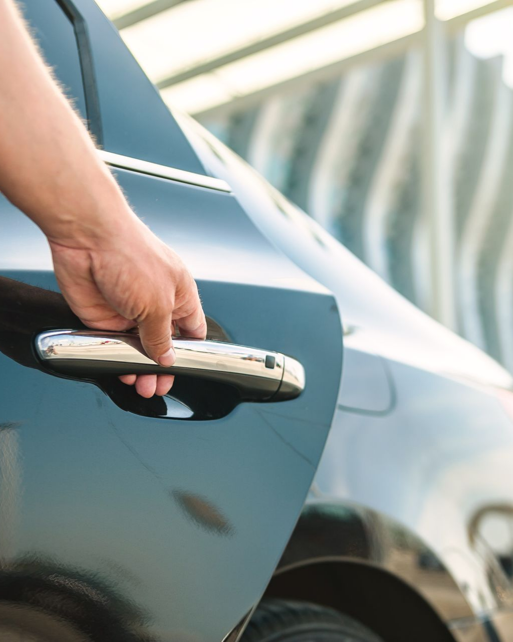 Ouverture manuelle d'une portière de voiture noire avec poignée chromée.