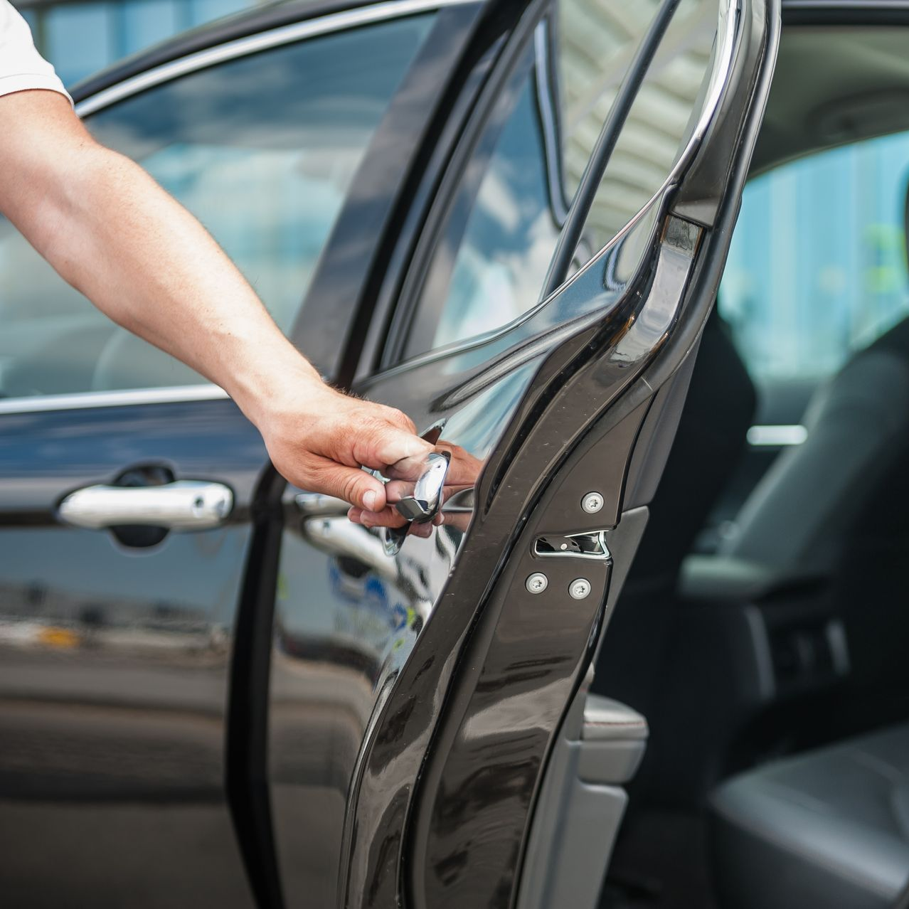 Une main ouvre la portière d'une voiture noire, dévoilant partiellement l'intérieur.