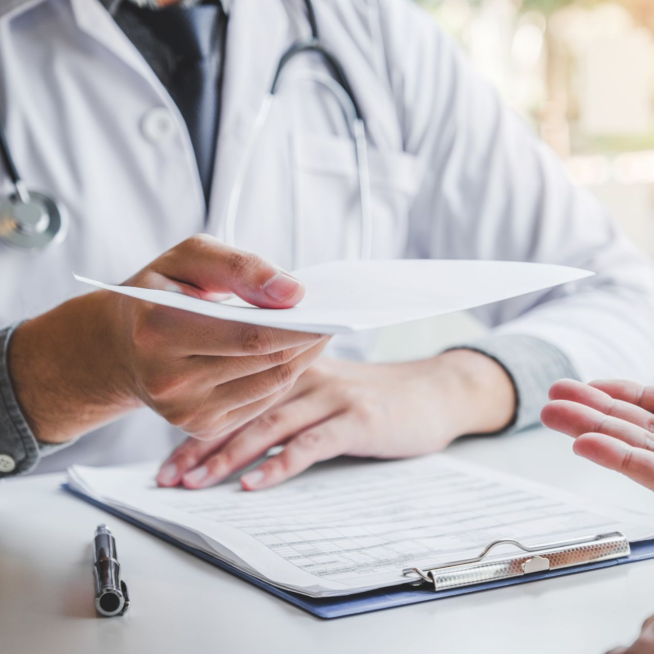 Un médecin remet des documents à un patient ; blouse blanche, stéthoscope et documents sur un bloc-notes sont visibles.