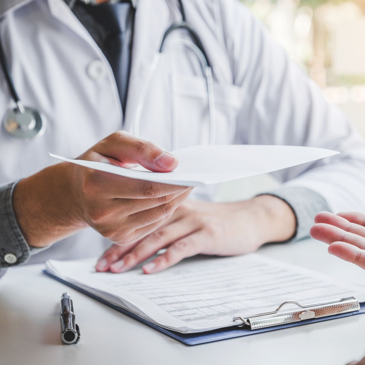 Un médecin en blouse blanche remet un document au patient assis à un bureau.