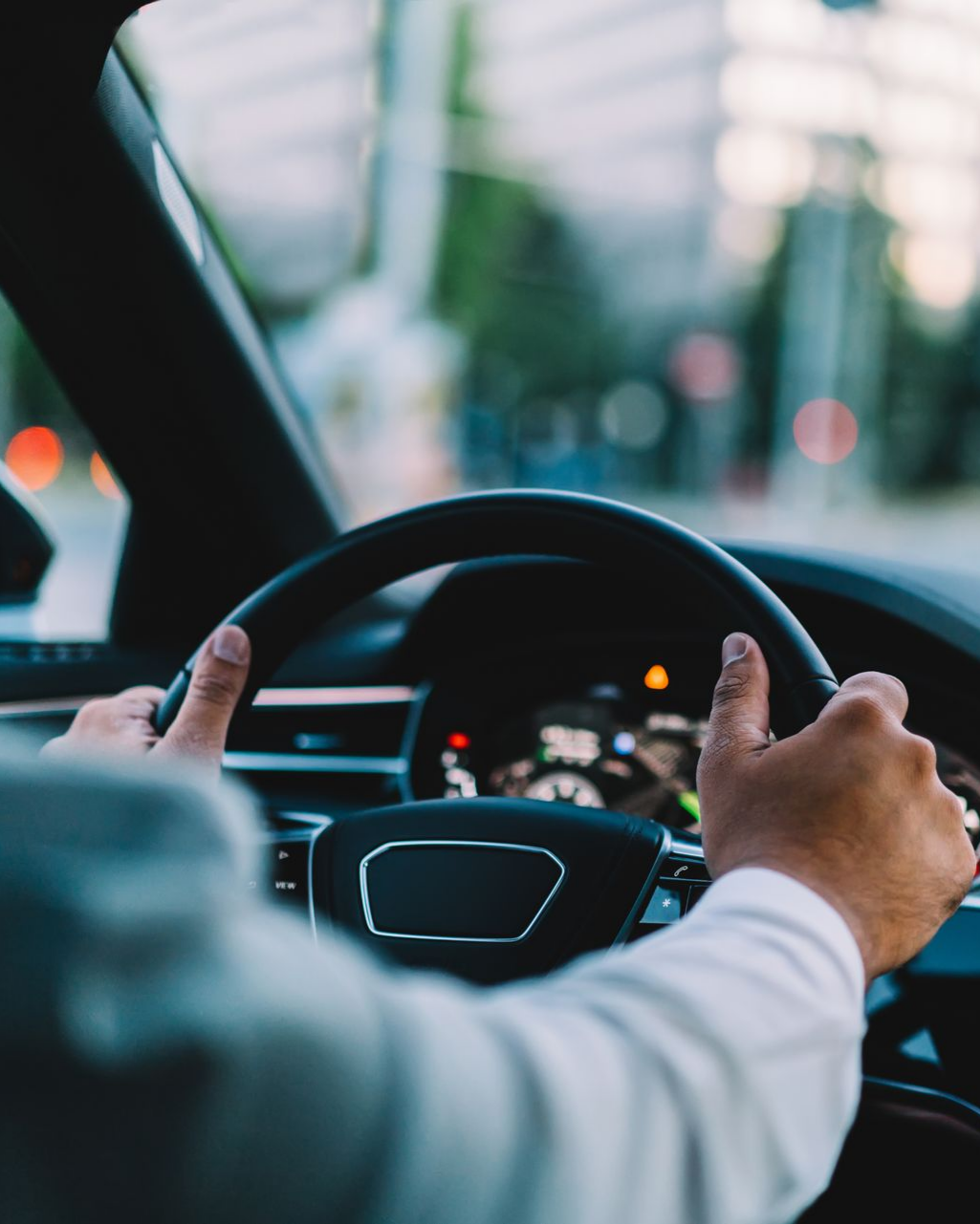 Des mains agrippées au volant d'une voiture, roulant dans une rue de la ville.
