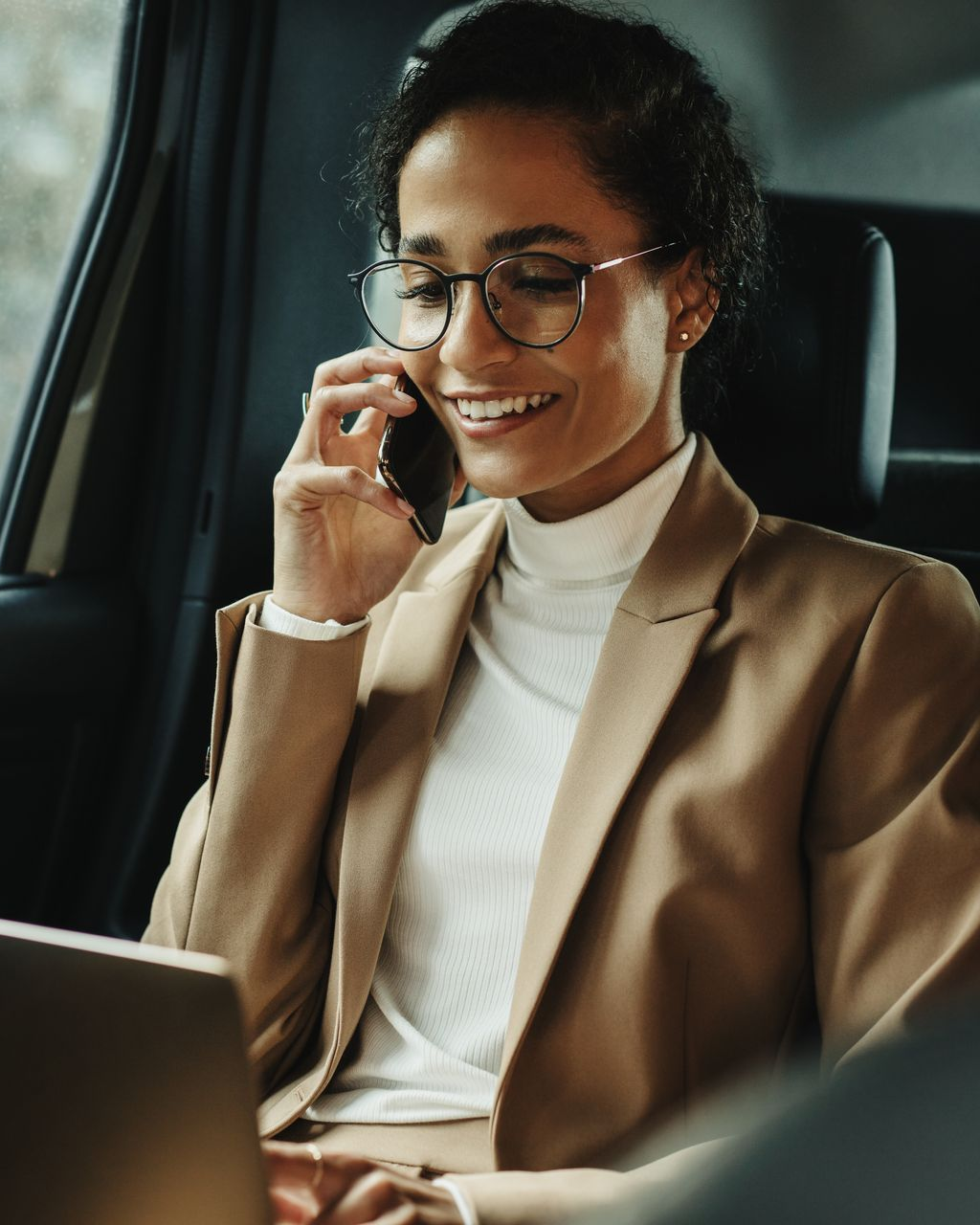 Une femme au téléphone dans une voiture avec un ordinateur  sur les genoux