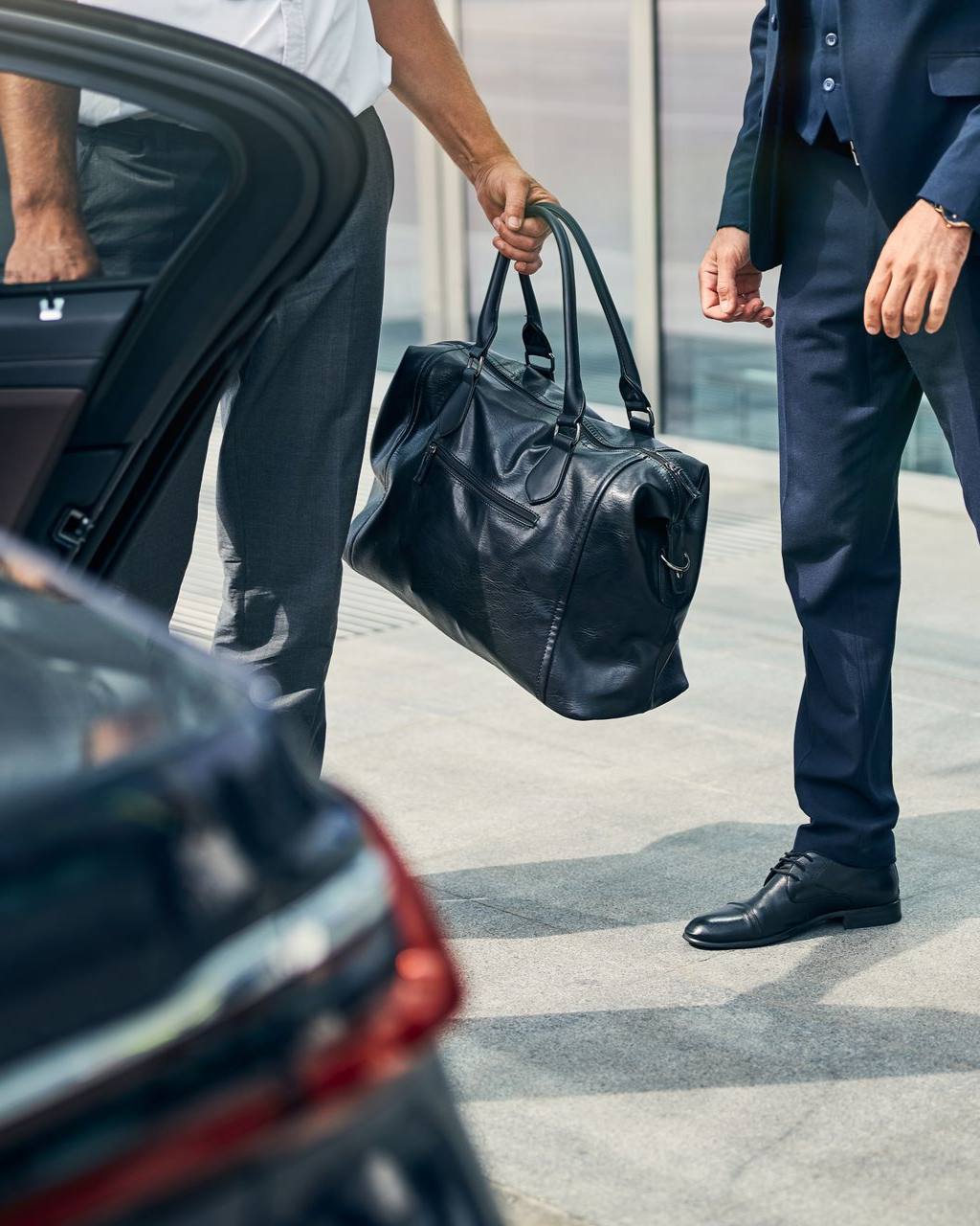 Un homme sort d'une voiture, un autre tient son sac de sport noir. Cadre moderne en extérieur.