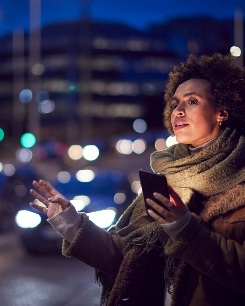 Une femme tenant un téléphone hèle un taxi dans une rue de la ville, la nuit.