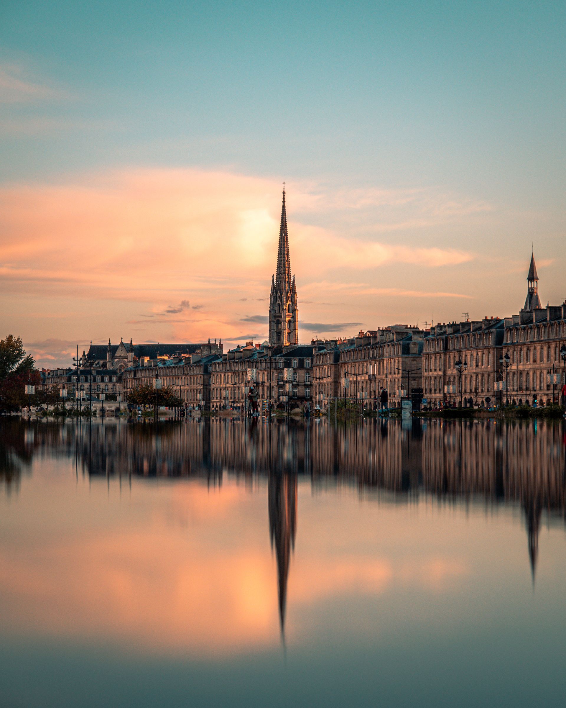 La silhouette de la ville se reflète dans l'eau calme au coucher du soleil ; ciel orange et bleu.