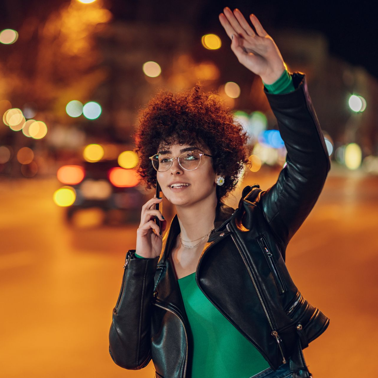 Une femme en veste de cuir hèle un taxi dans une rue de la ville, la nuit.