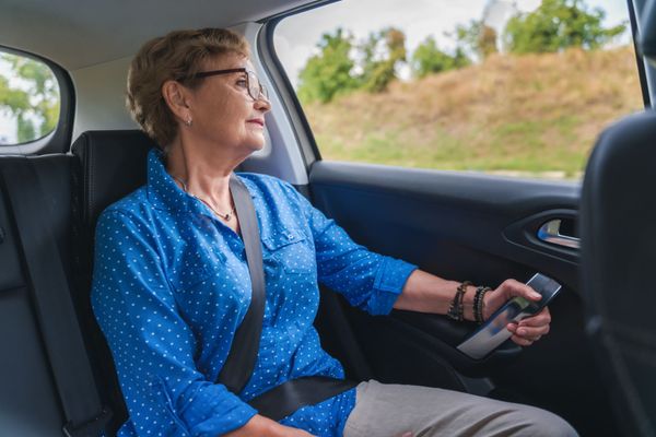 Femme en voiture, regardant par la fenêtre, portant des lunettes et une chemise bleue, ceinture de sécurité bouclée.