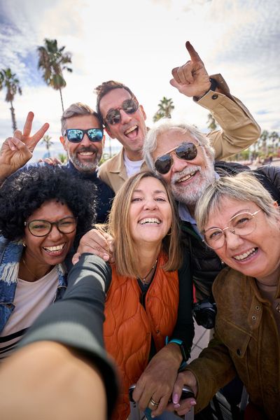 Selfie de groupe en extérieur ; personnes souriantes, journée ensoleillée, palmiers en arrière-plan.