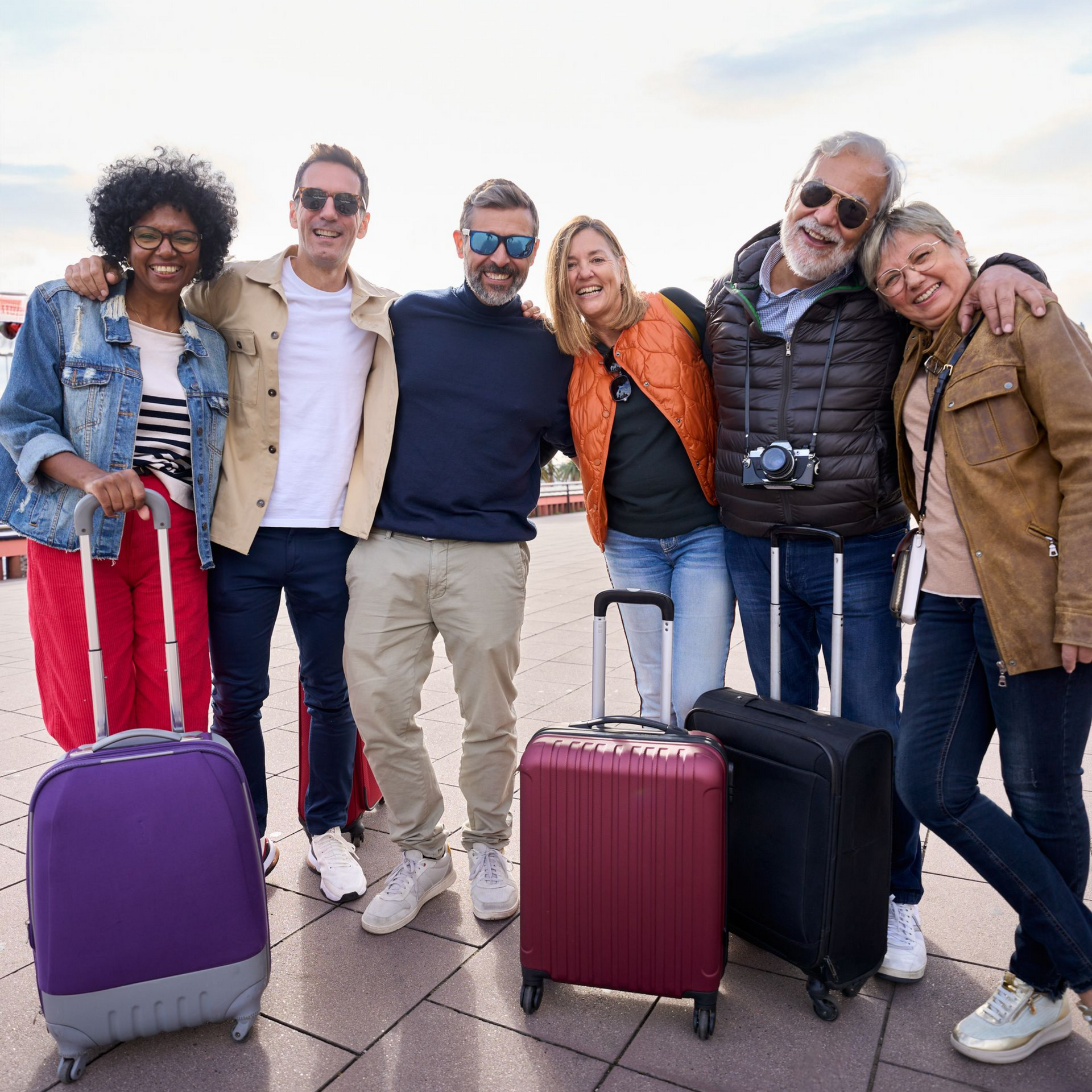 Groupe de personnes avec des bagages, souriantes, posant à l'extérieur.