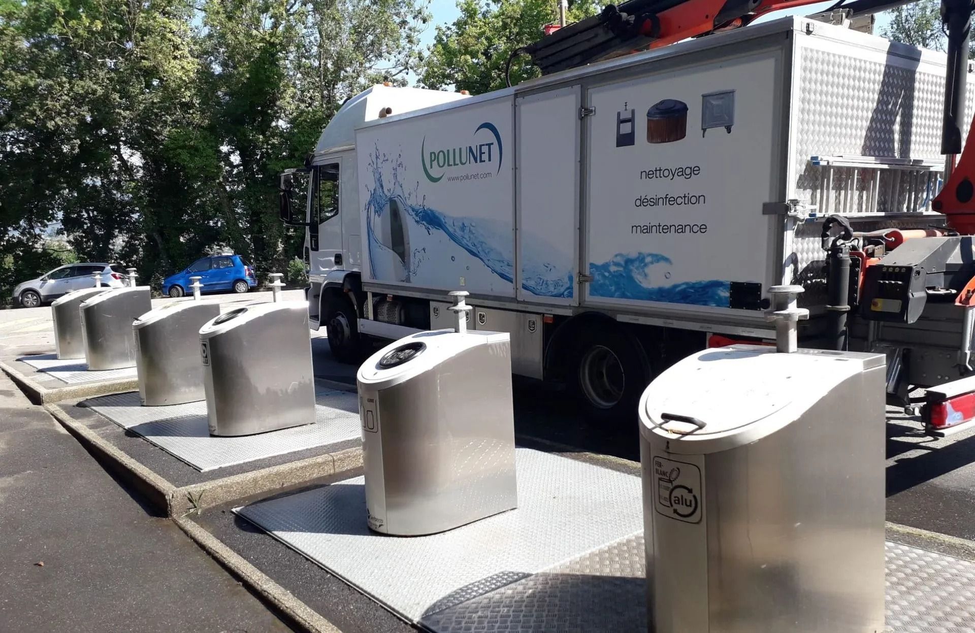 Un camion de recyclage à côté de plusieurs bacs de recyclage argentés sur une plate-forme, sous un ciel bleu.