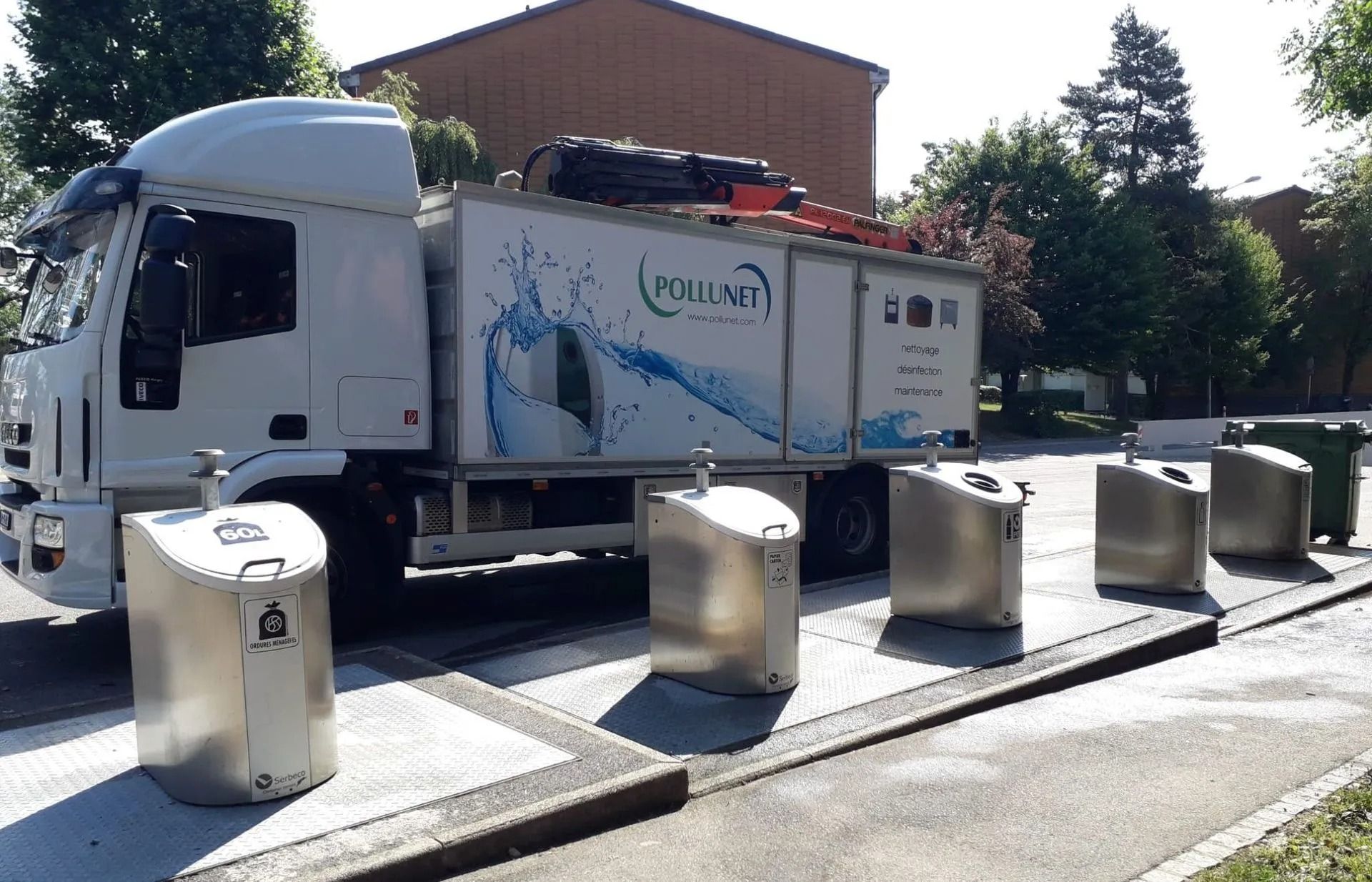 Un camion blanc à côté de plusieurs bacs de recyclage argentés.