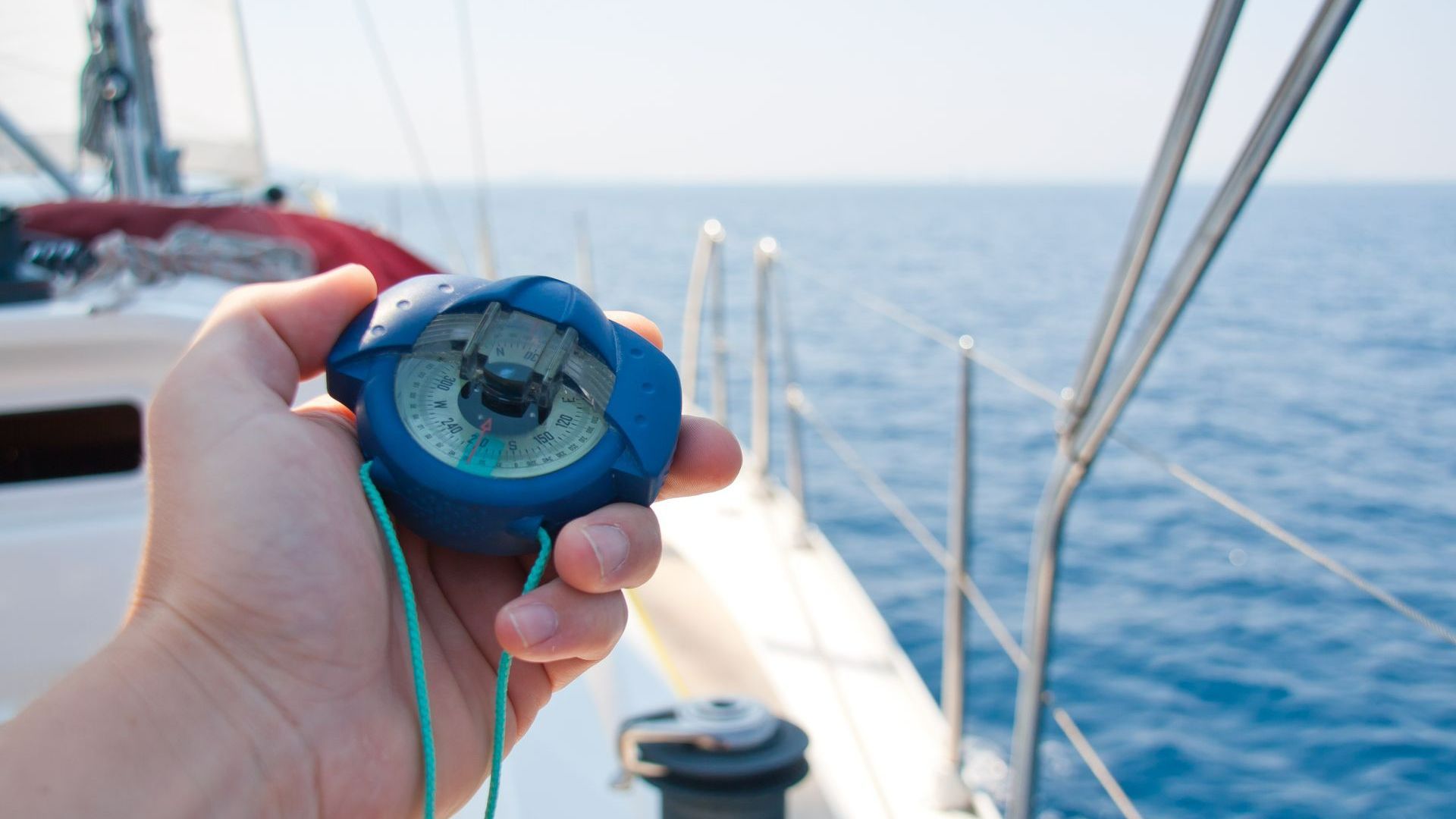 Compas de relèvement bleu tenue par une main sur le pont d'un bateau blanc - permis hauturier