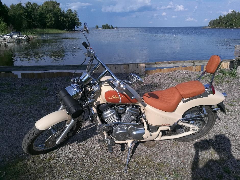 Oranssin ja kermanvärinen moottoripyörä pysäköitynä sorarannalle järven rannalle sinisen taivaan alle