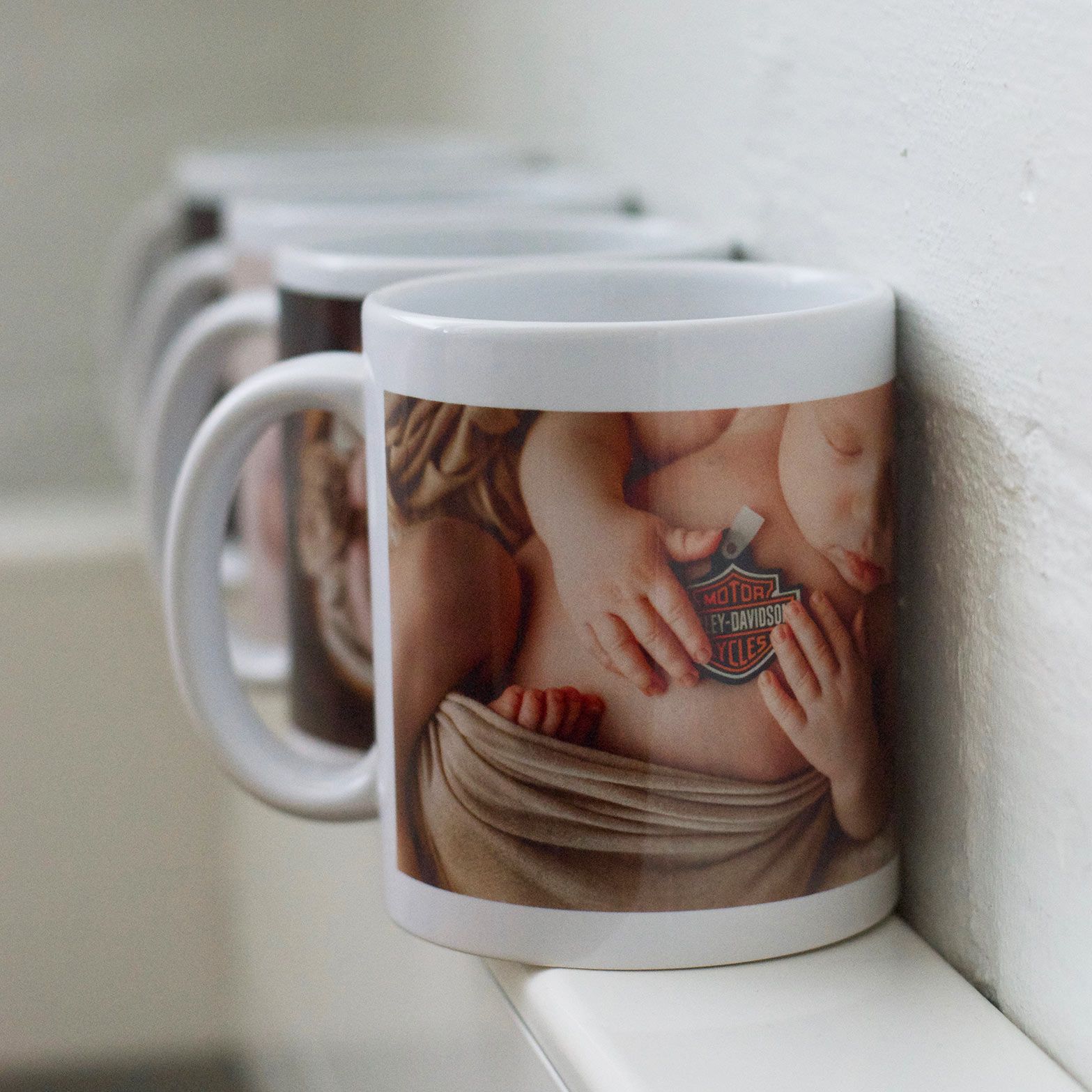 Rivi valkoisia keramiikkamukeja hyllyllä, joista jokaisessa on painettu lyhyt torso-kuvio ja vaakunatunnus.