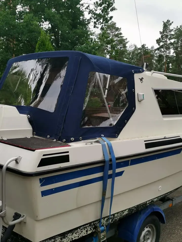 Pieni valkoinen vene, jossa on laivastonsininen kangaspeite, trailerissa ulkona