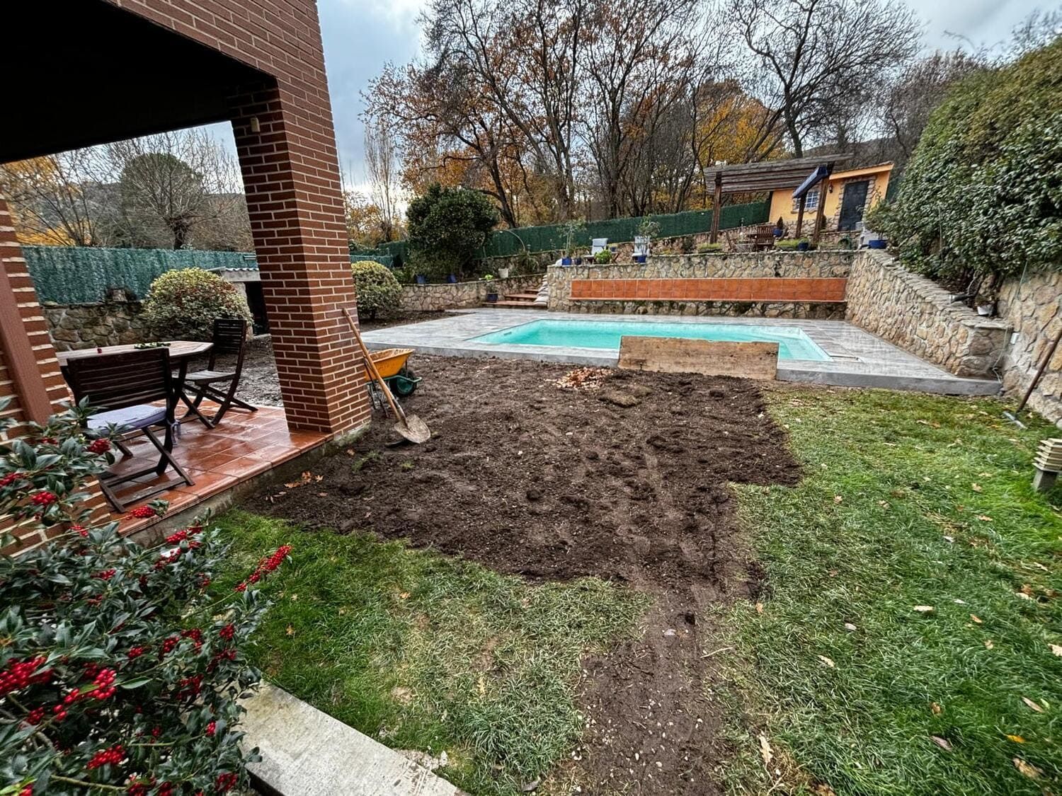 Patio trasero con piscina, patio y césped recién labrado. Cielo nublado.