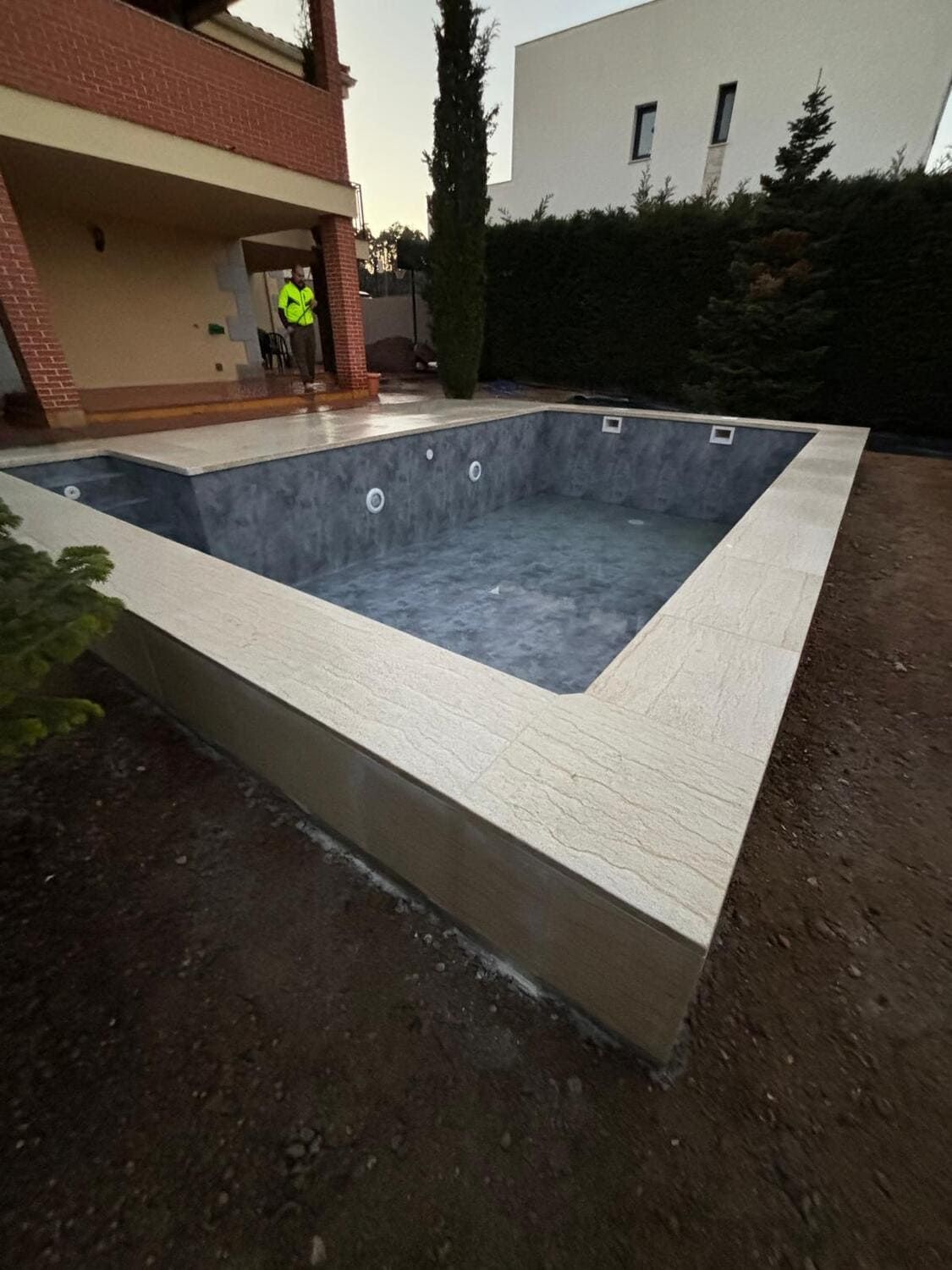 Piscina rectangular vacía con marco de azulejos de color claro e interior gris oscuro, ubicada en un patio trasero.