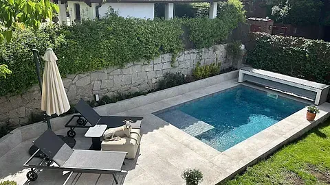 Una pequeña piscina en un patio trasero con sillas y sombrillas.