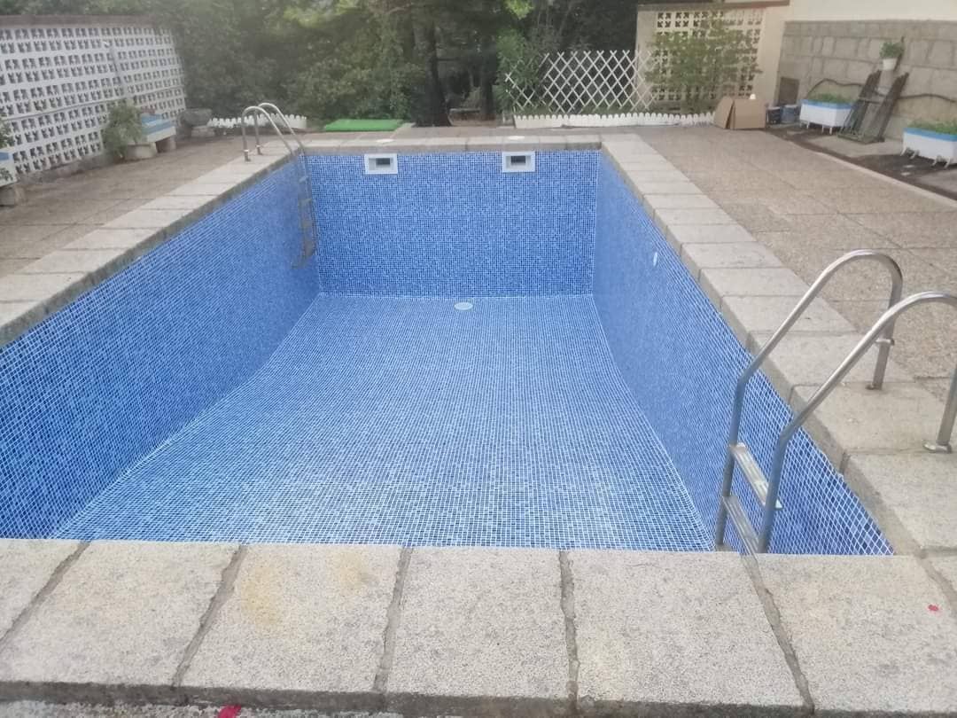 Piscina rectangular vacía con interior de azulejos azules, escalera de metal y marco de piedra.