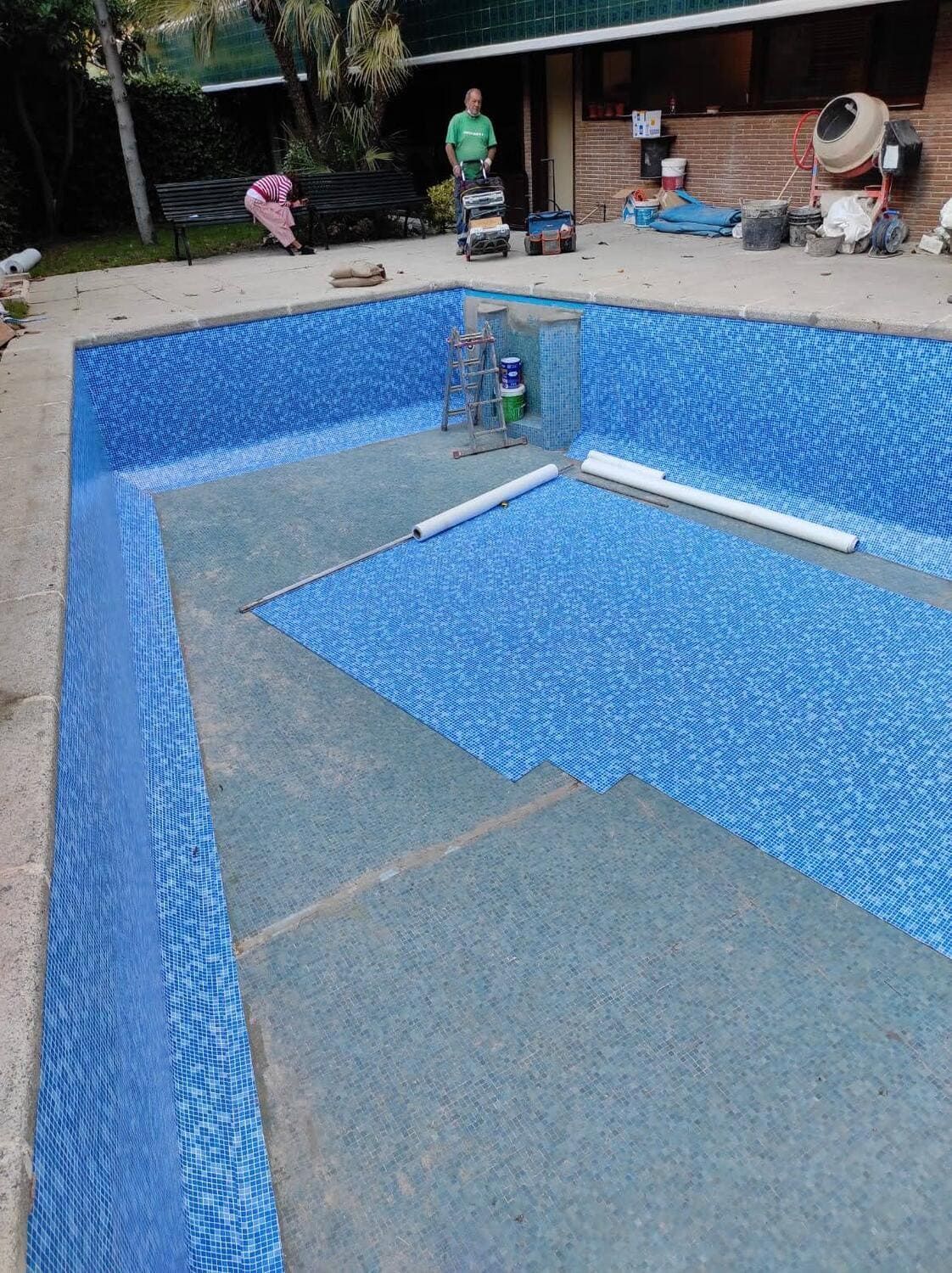 Piscina parcialmente embaldosada; una persona al fondo; entorno al aire libre.