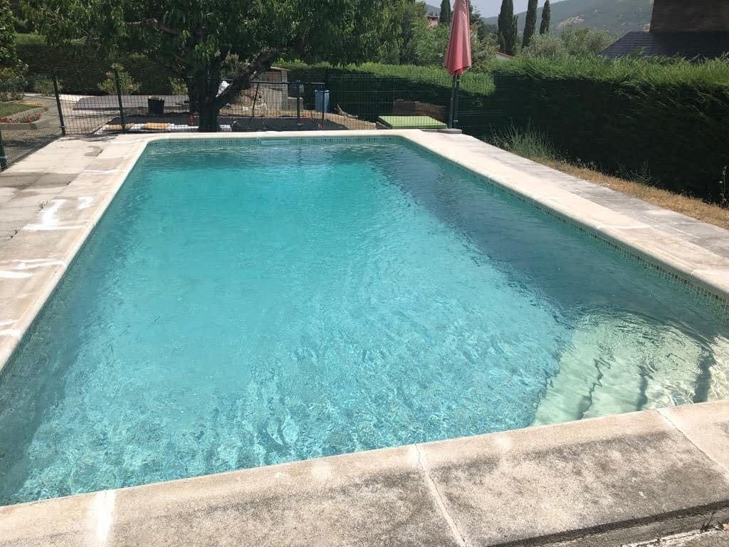 Piscina rectangular de agua turquesa, rodeada de pavimento de piedra y vegetación.