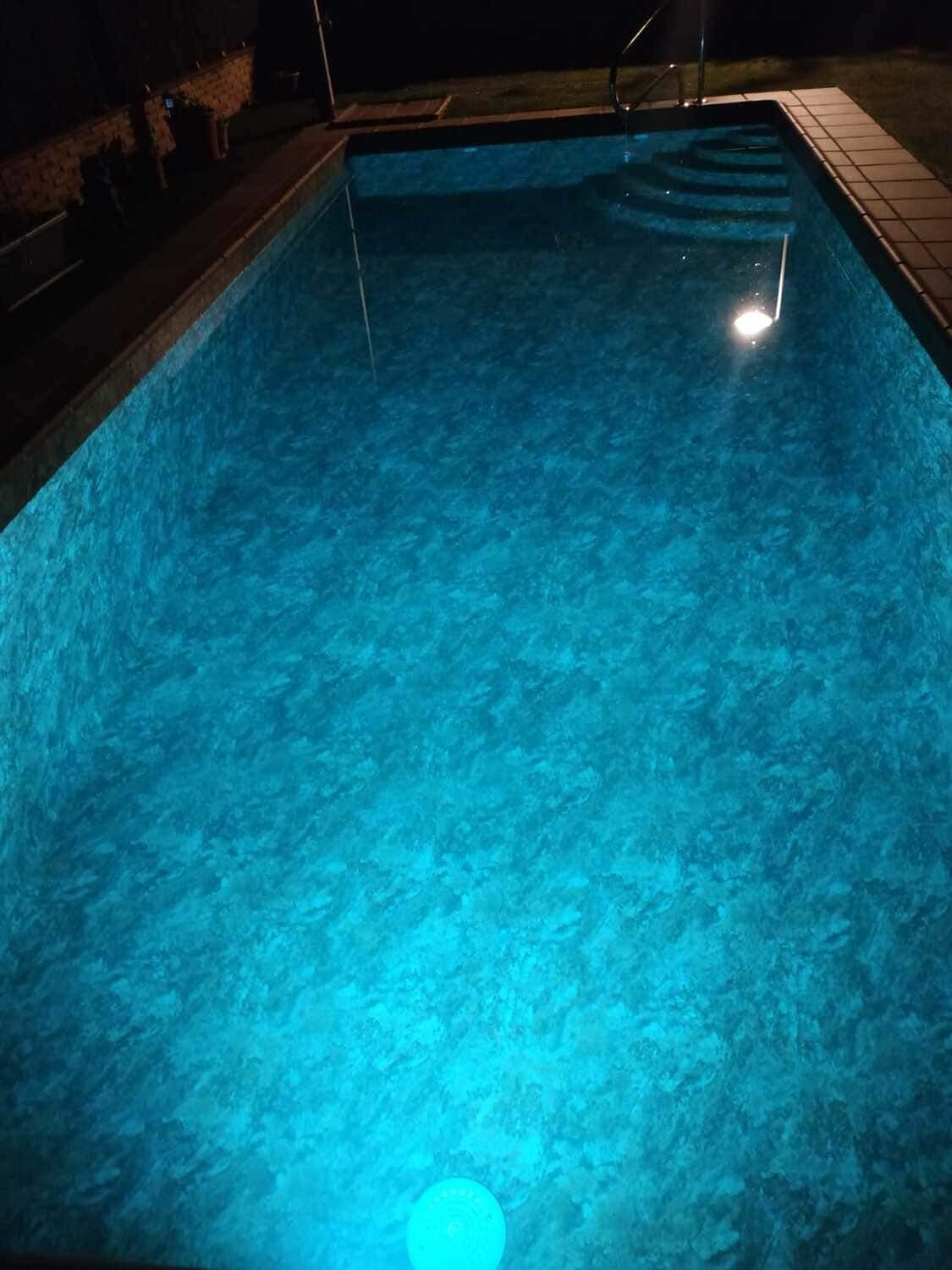 Piscina nocturna, iluminada color turquesa, escalones visibles.