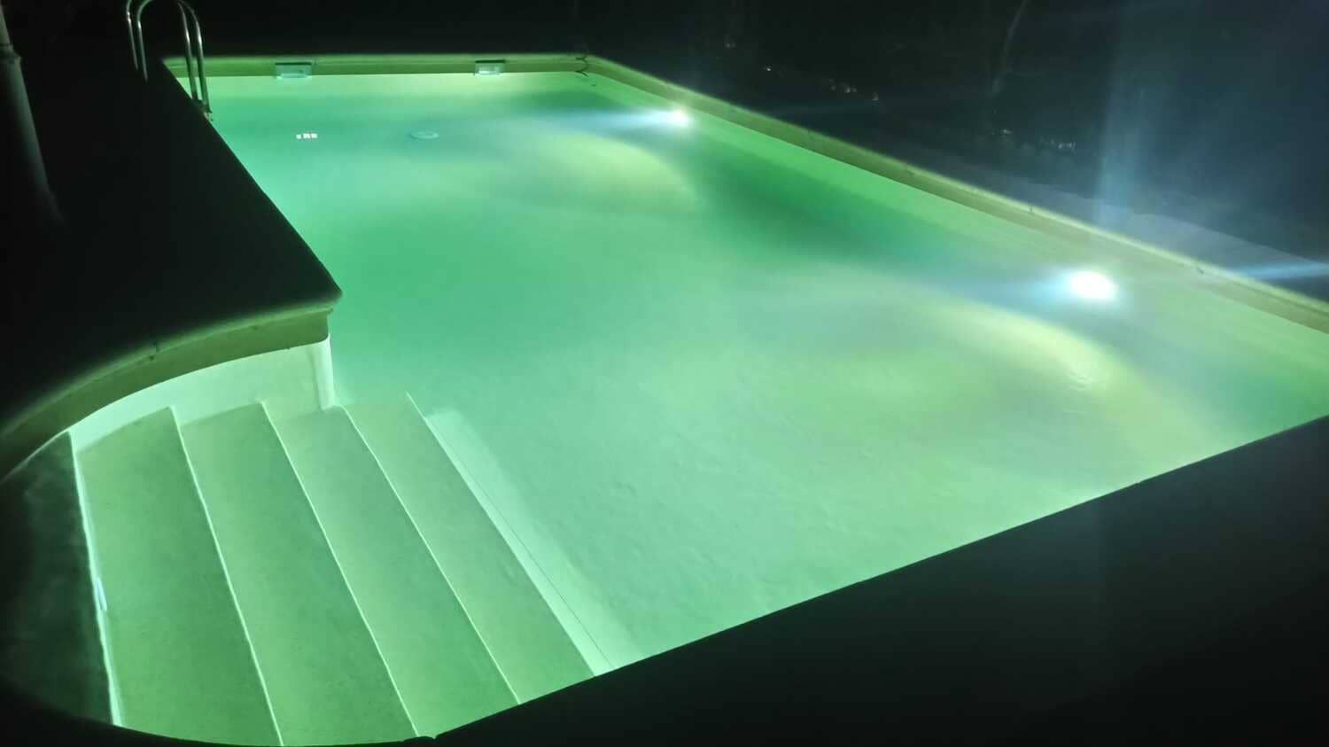 Piscina verde iluminada con escalones por la noche.