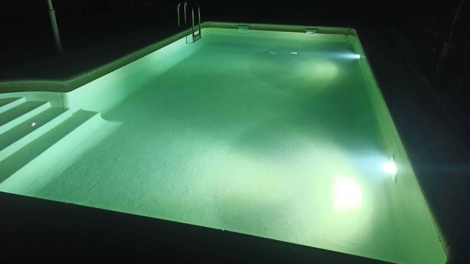 Piscina rectangular iluminada por la noche, la luz verde se refleja en el agua, escalones en la esquina.