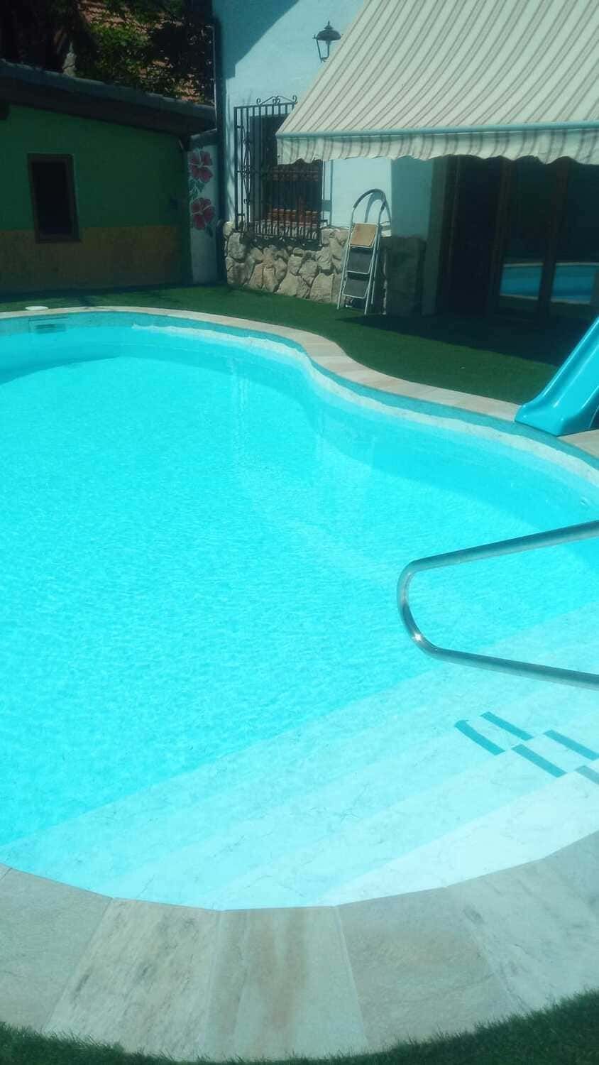 Piscina con agua azul y césped verde circundante, junto a una casa blanca.