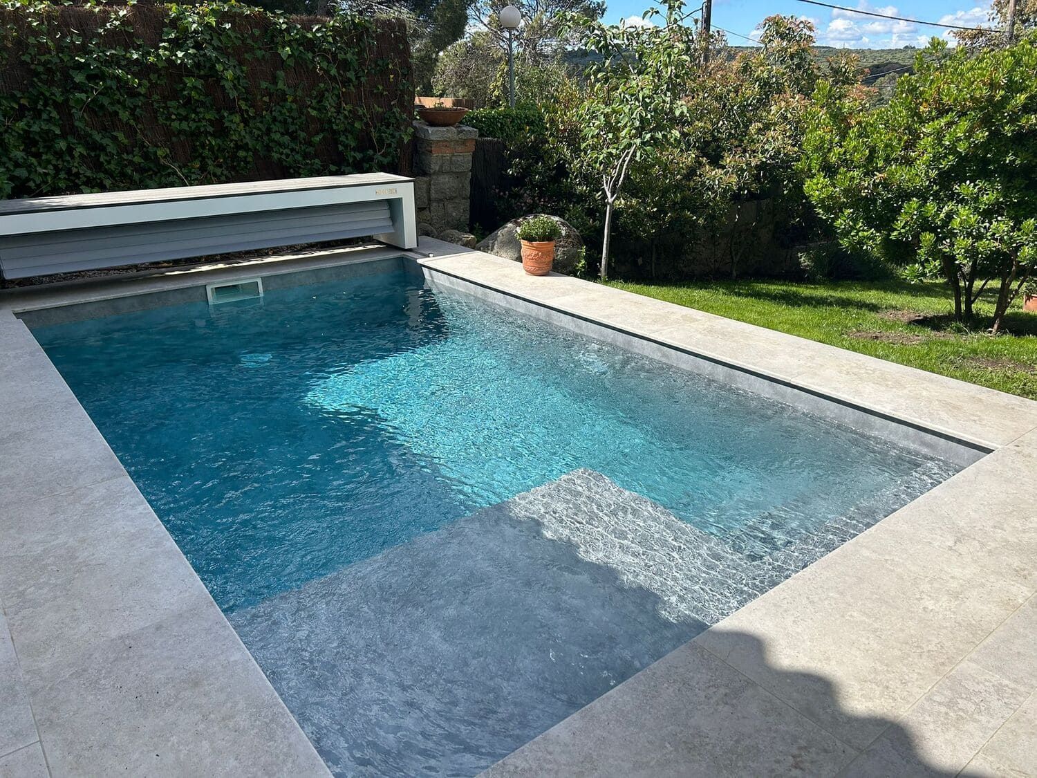Una piscina rectangular de agua azul clara, rodeada de hormigón y vegetación.