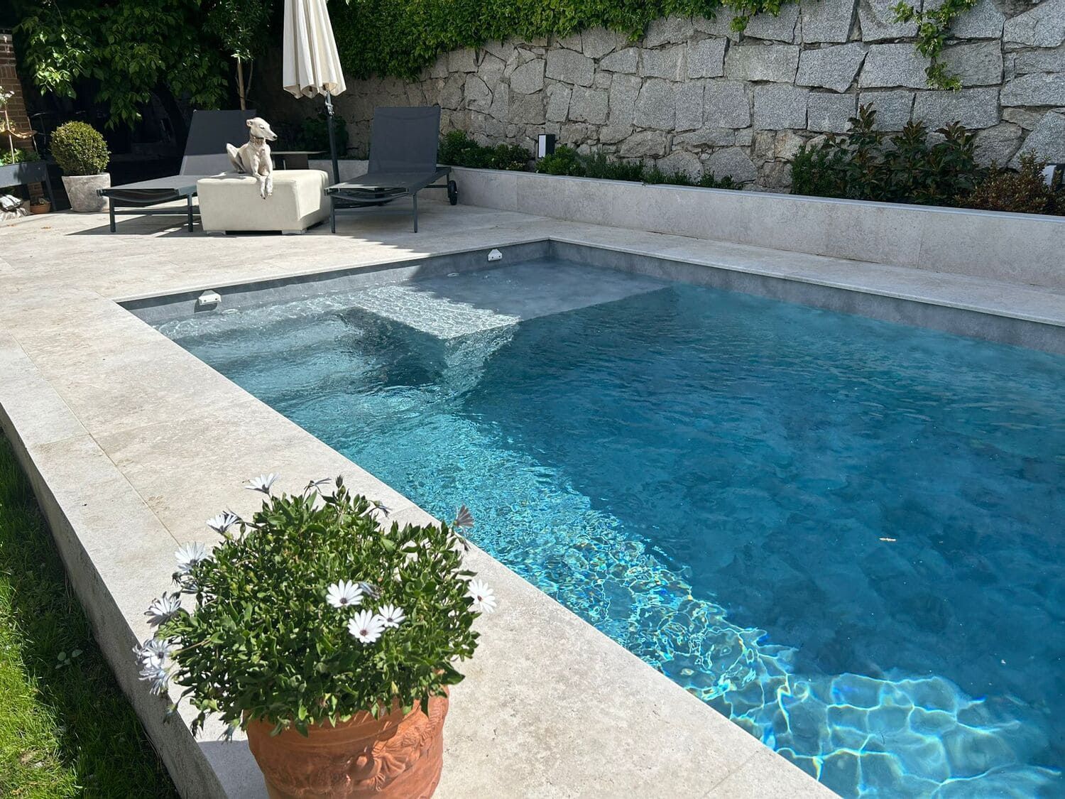 Una pequeña piscina de color azul claro con escalones, rodeada de piedras y vegetación.