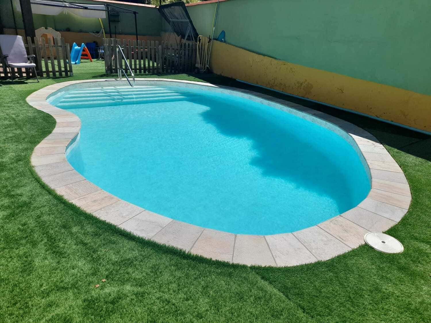 Una piscina en forma de riñón con agua azul rodeada de adoquines de piedra y césped verde.