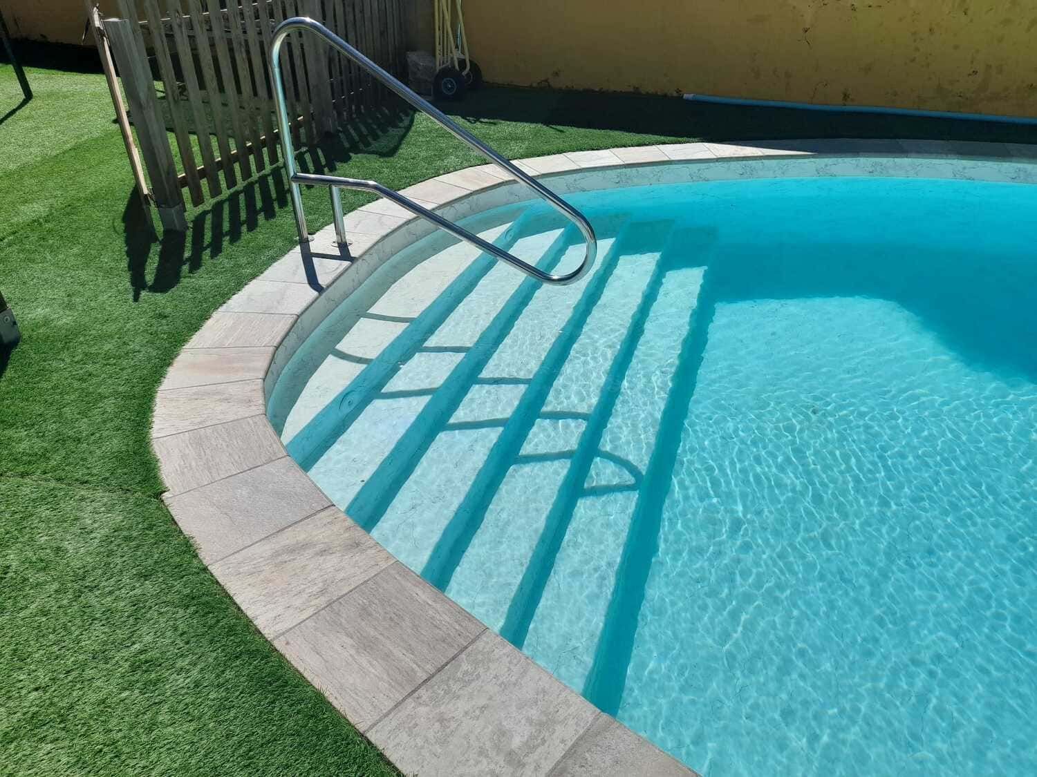 Piscina con escalones, pasamanos y agua azul cristalina.