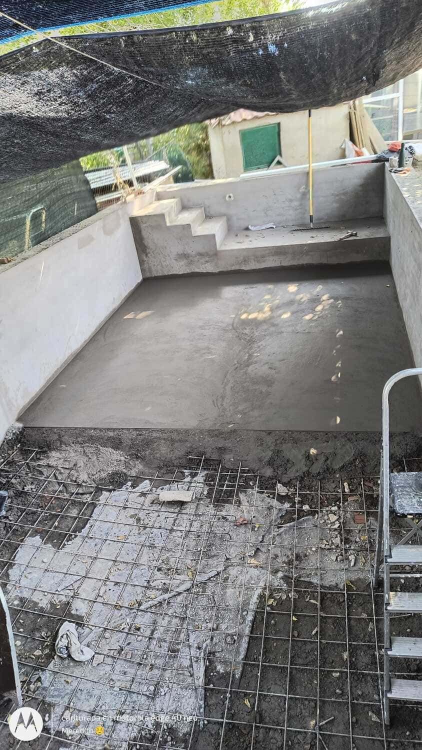 Construcción de piscina de hormigón en curso con escalones. Hormigón gris, varillas de refuerzo, escalones y alrededores.